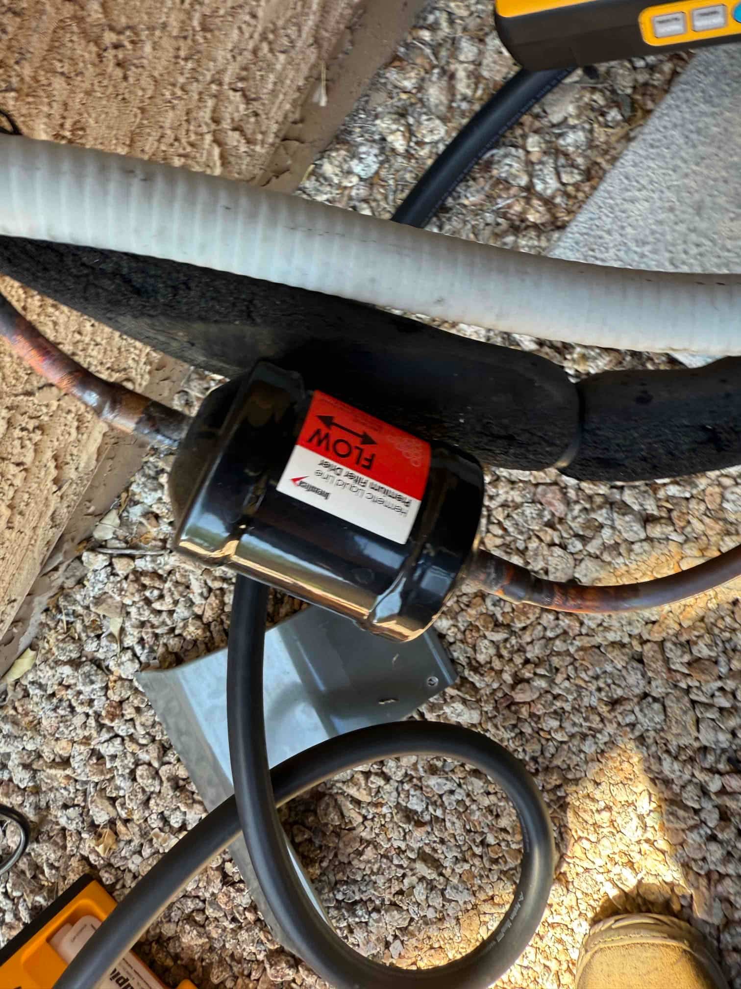 Inline liquid-line filter drier installed on copper refrigerant tubing, labeled with a red flow direction arrow.