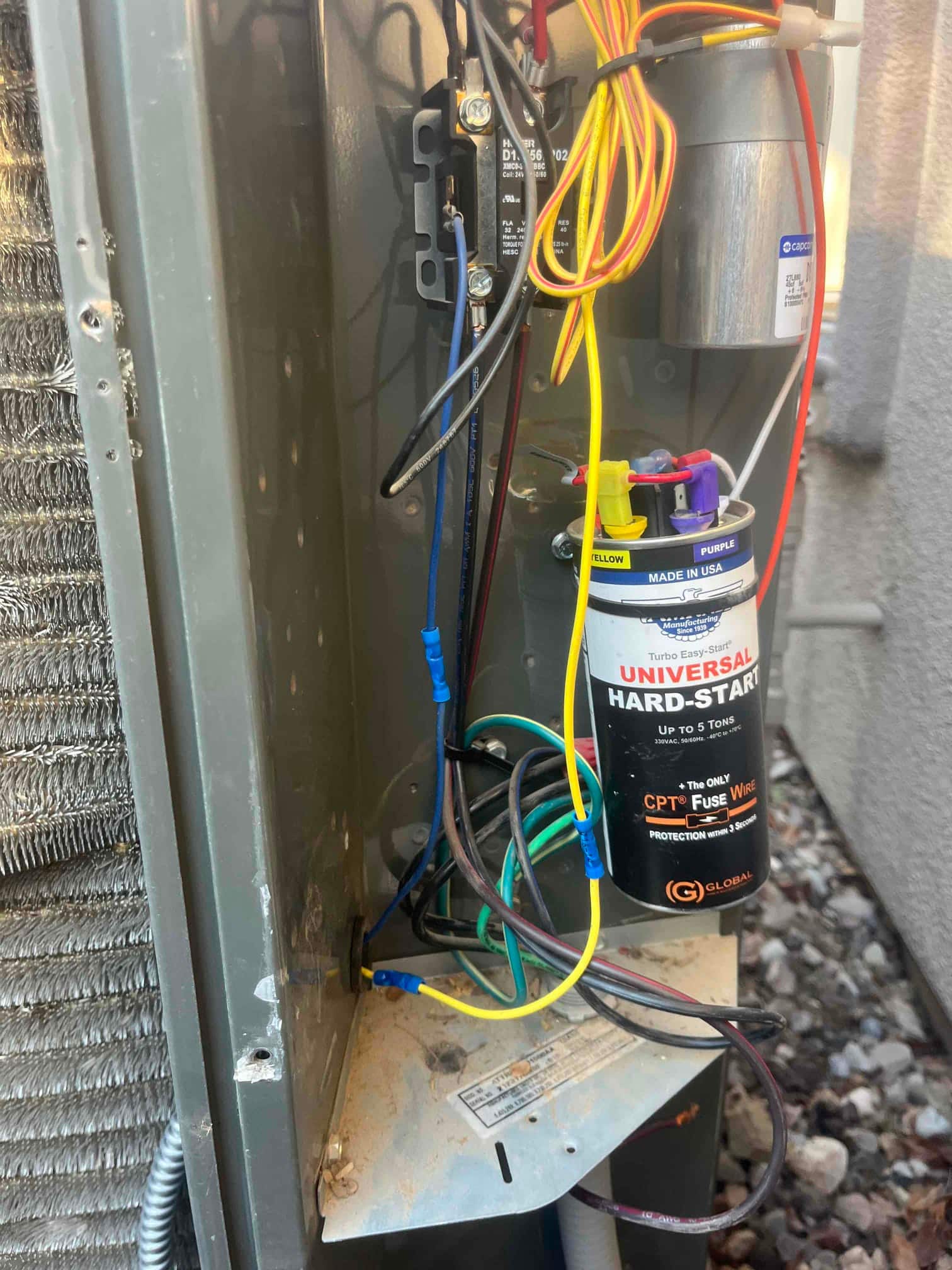 Outdoor condenser control compartment showing hard-start kit, run capacitor, contactor, and connected wiring inside the unit.