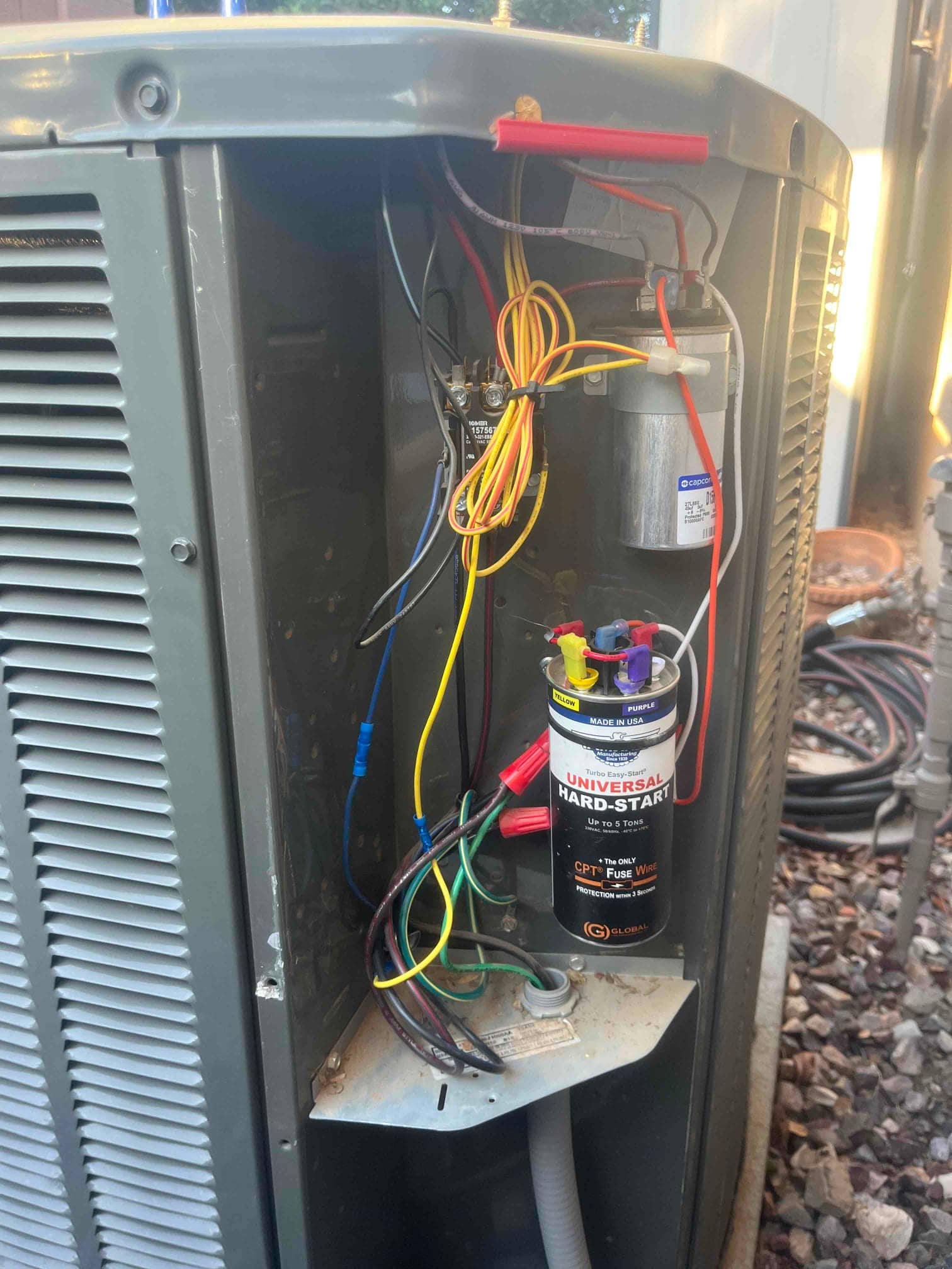Outdoor condenser control compartment open, showing dual-run capacitor, contactor, installed hard-start kit, and connected wiring harnesses.