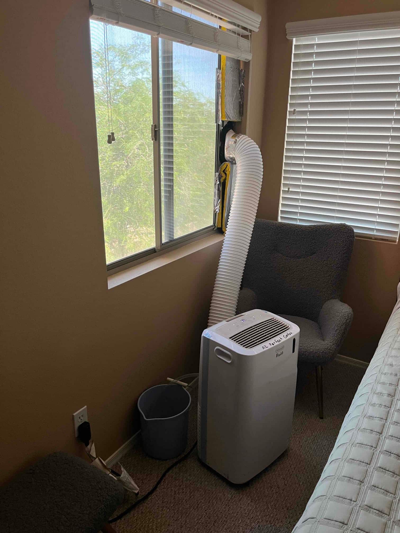 Portable air conditioner sits beside bed with flexible exhaust hose vented through modified window panel.
