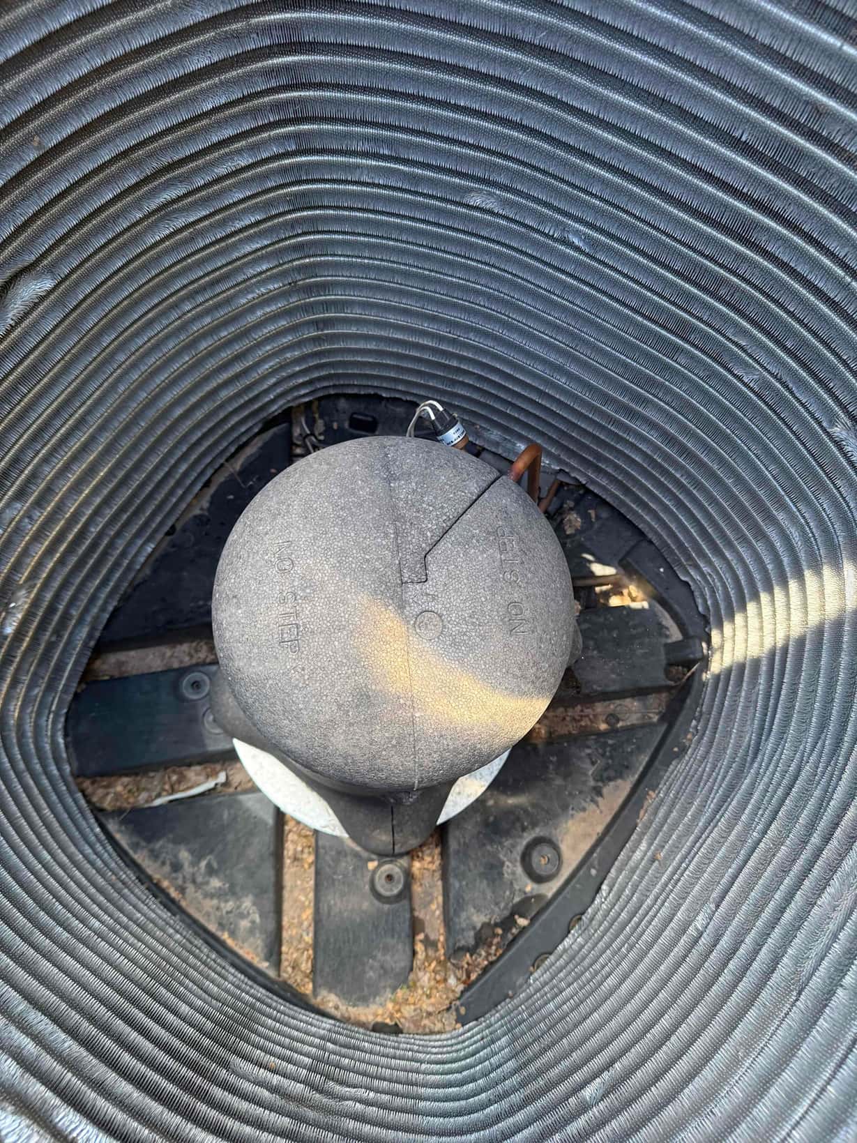 Top-down view inside a residential outdoor condenser, showing the central compressor with sound blanket and surrounding coil fins.