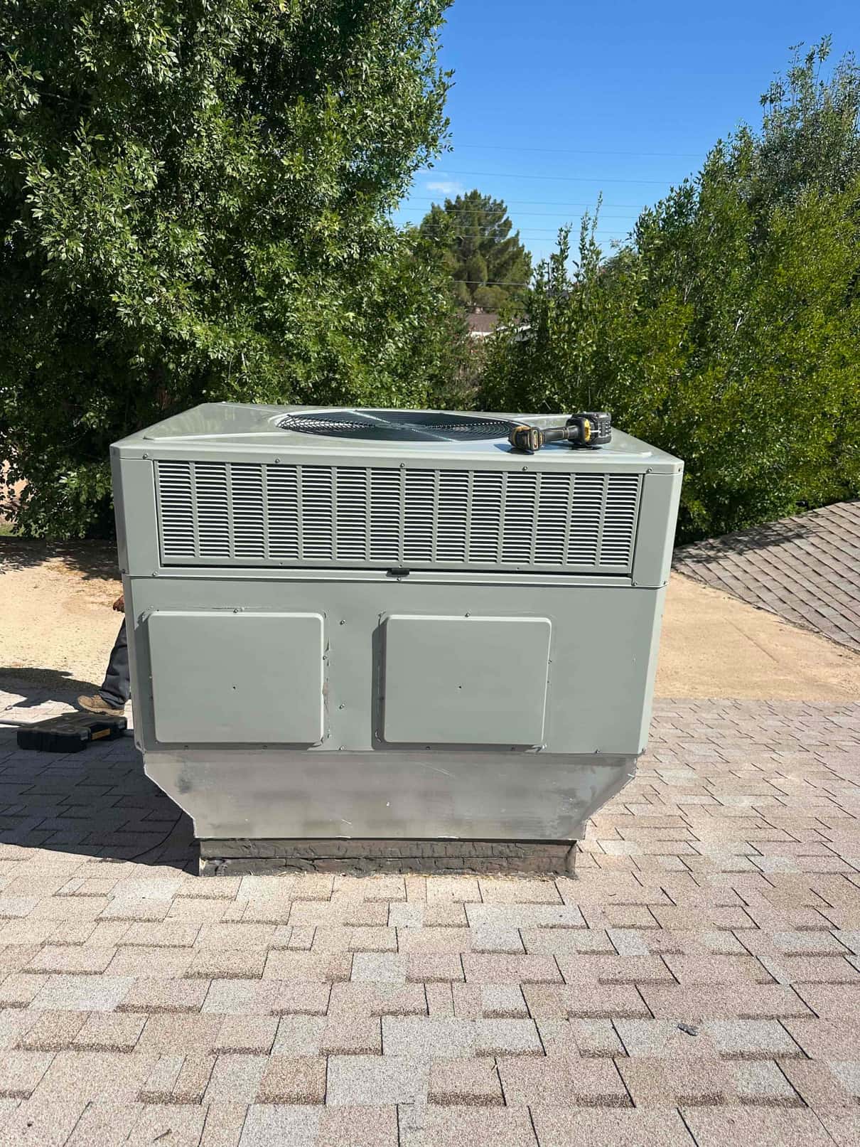 New rooftop package HVAC unit set on curb adapter with sealed base, surrounded by roofing shingles and tools nearby.