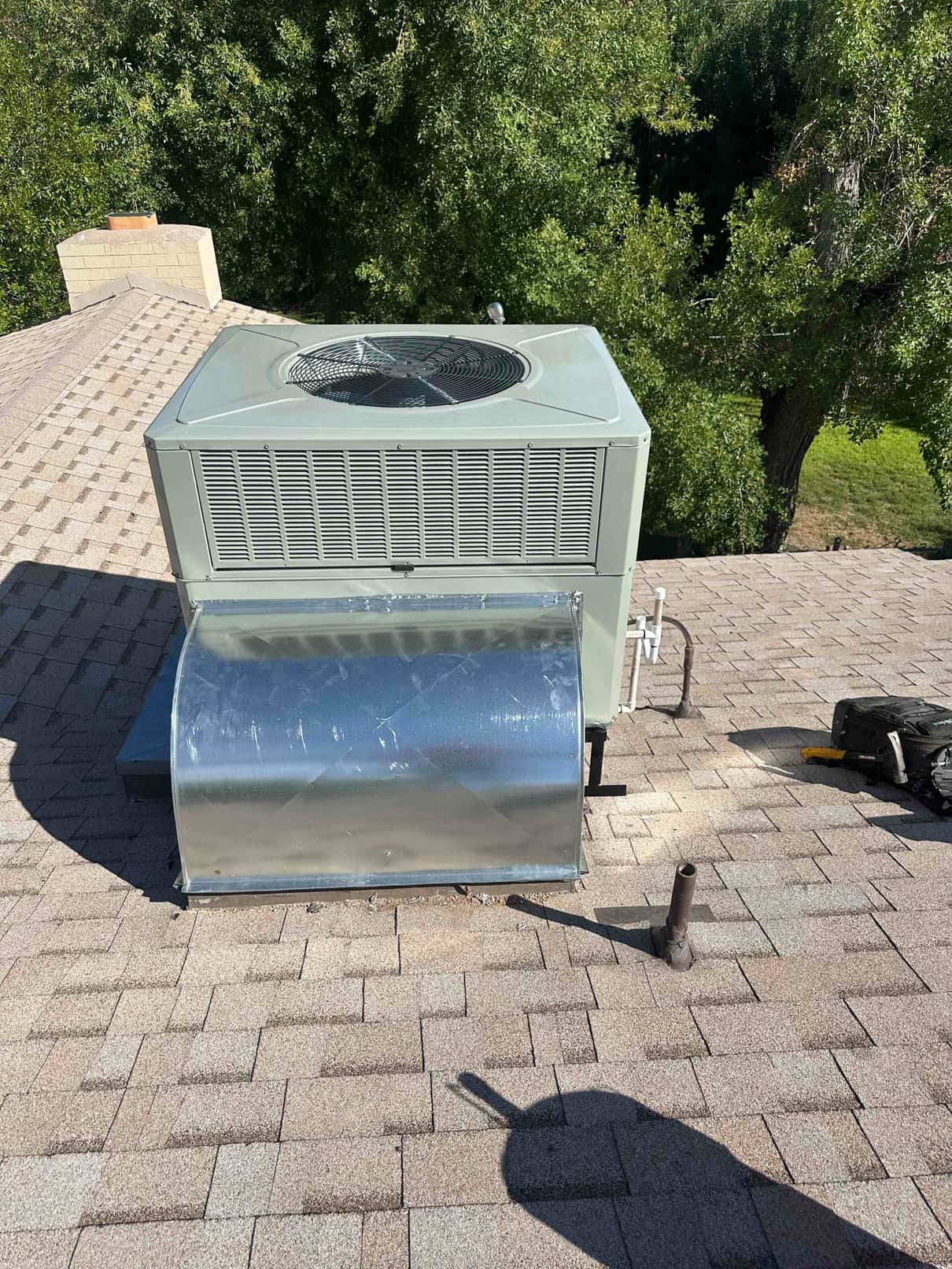 Rooftop packaged HVAC unit newly installed on shingles with sheet-metal curb and duct transition sealed to the roof.