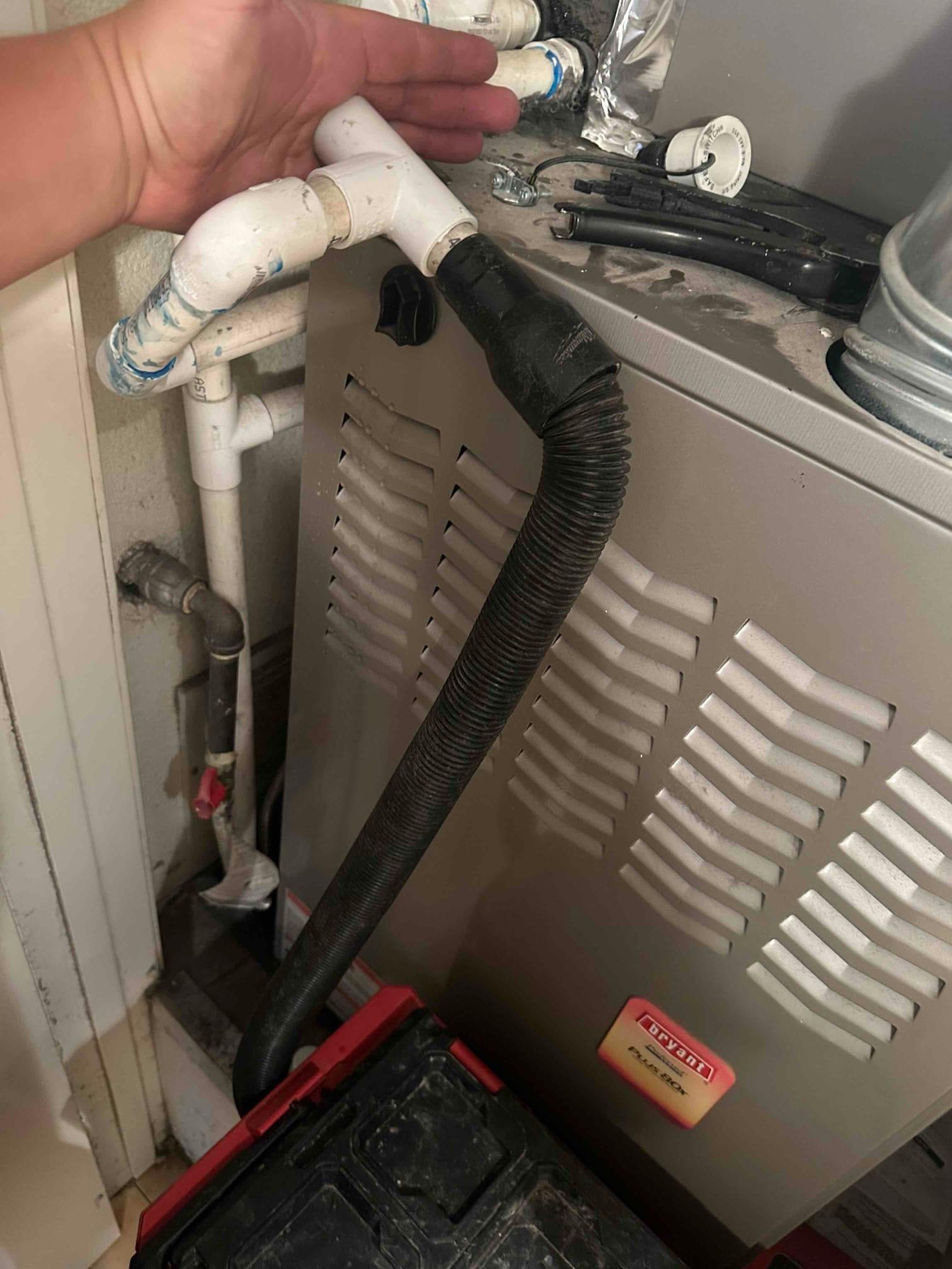 Furnace cabinet with PVC condensate drain piping and flexible black hose, technician hand above elbow fitting.