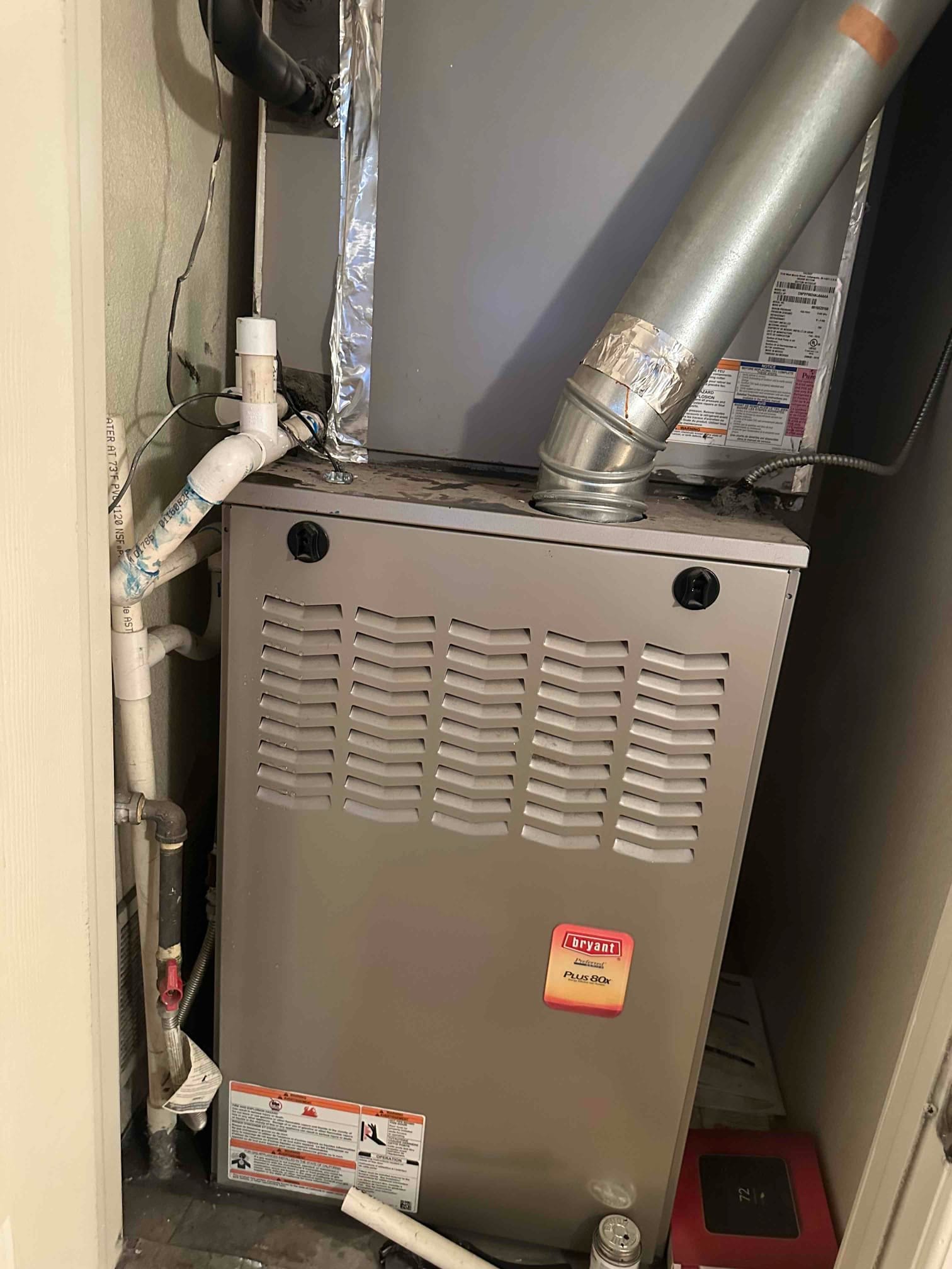 Gas furnace and evaporator coil in closet, with flue, condensate drain piping, and service labels visible.