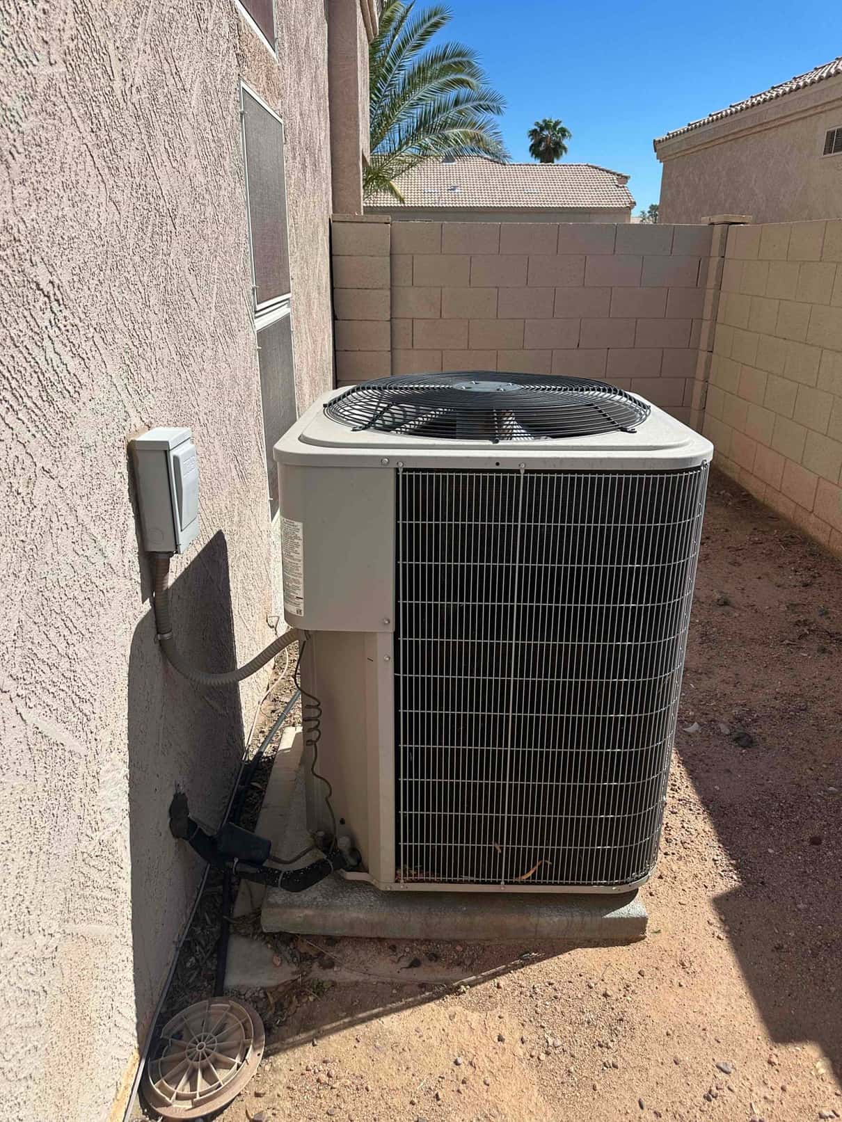Outdoor air conditioner condenser on a concrete pad beside the house, with insulated refrigerant lines and nearby service disconnect.