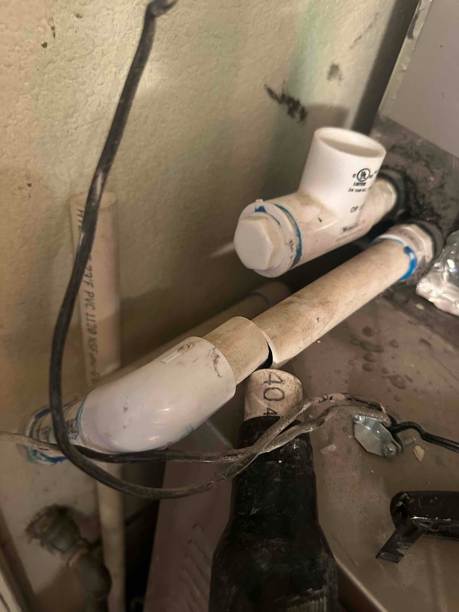 PVC condensate drain piping with tee cleanout and elbow routed over the indoor unit cabinet.