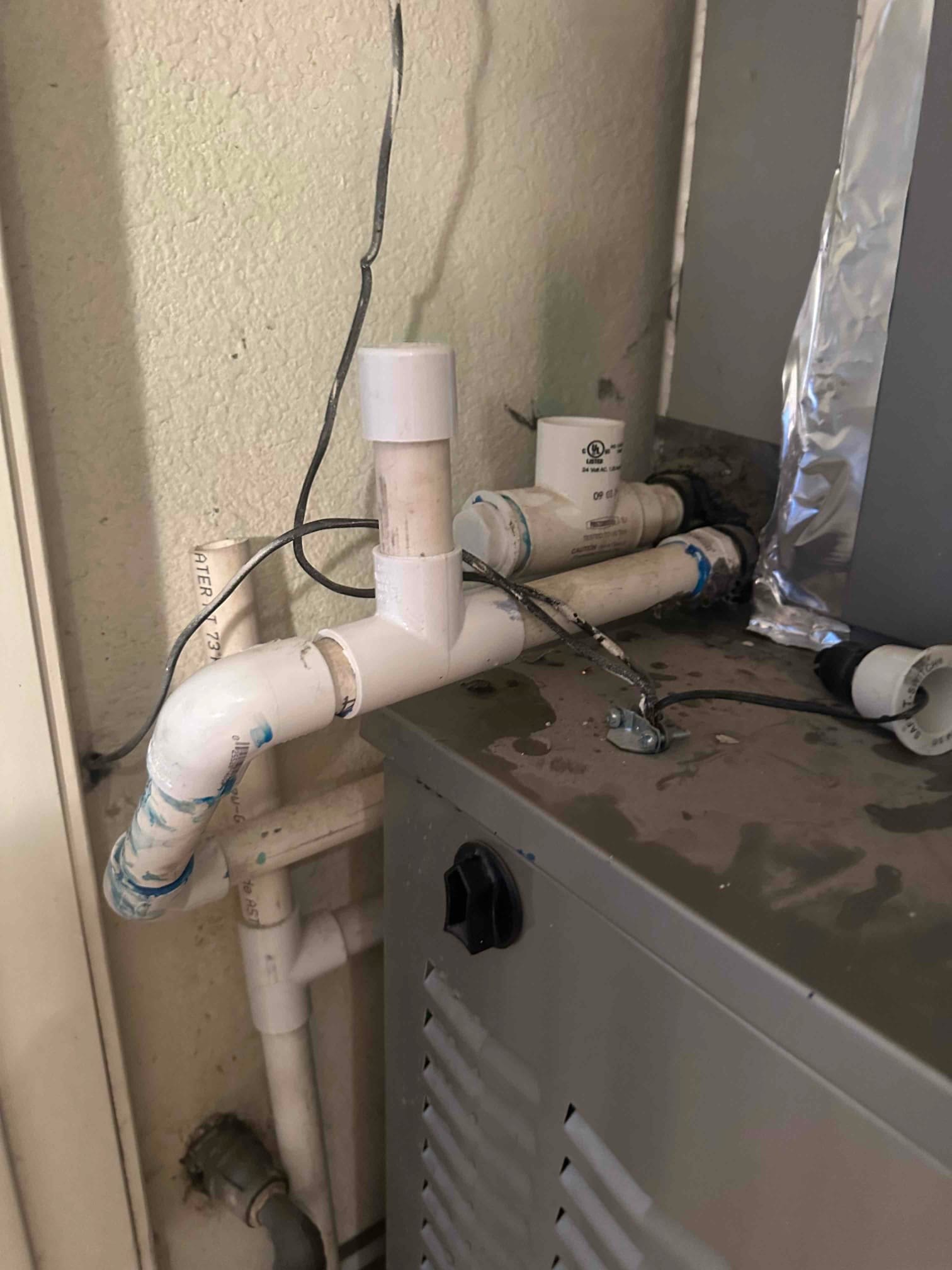 PVC condensate drain piping with trap and vent connected to the indoor unit cabinet, with water spots on the top.