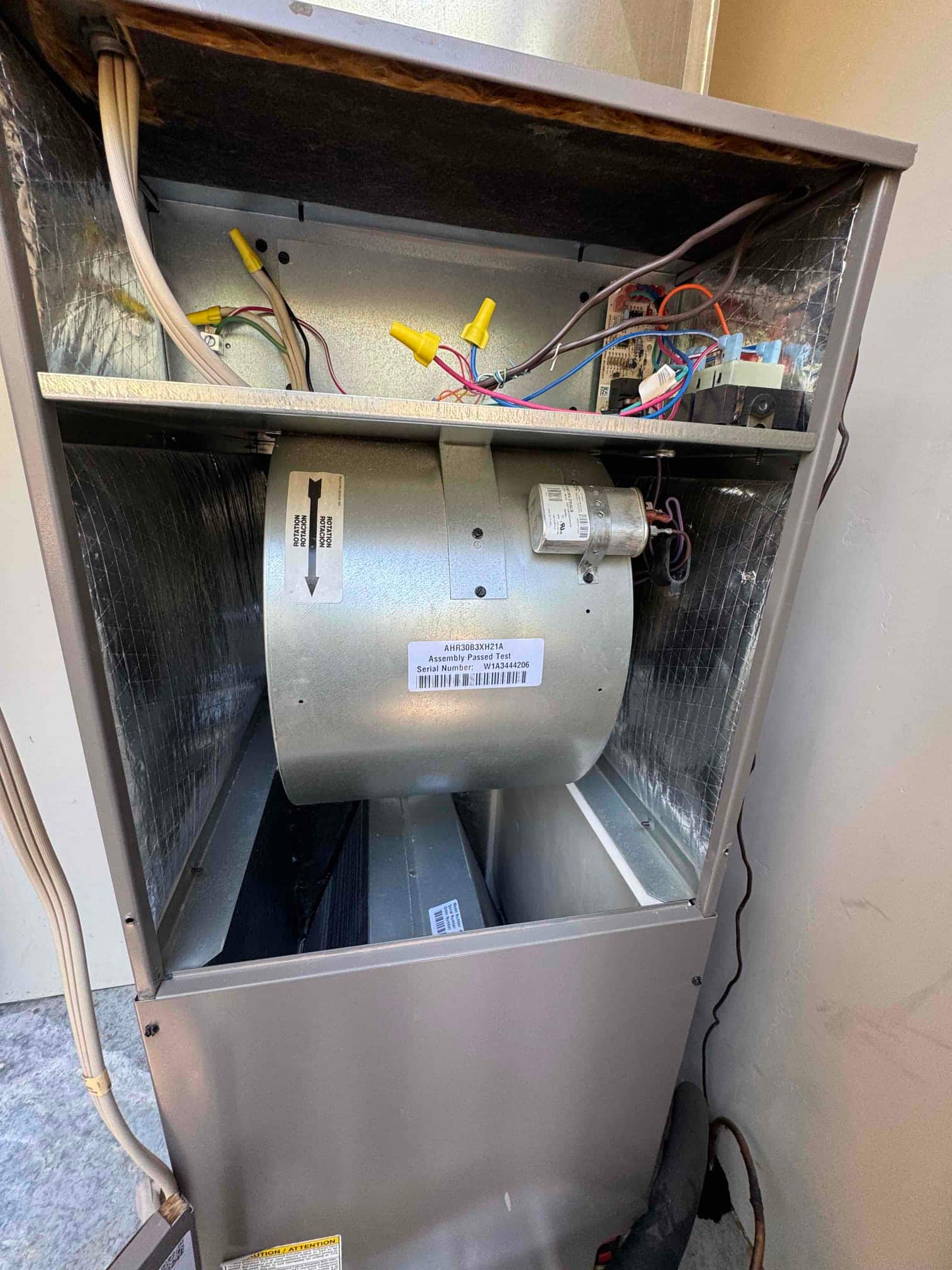 Air handler compartment open, showing blower wheel and motor with mounted capacitor, control wiring with wire nuts, and evaporator coil below.