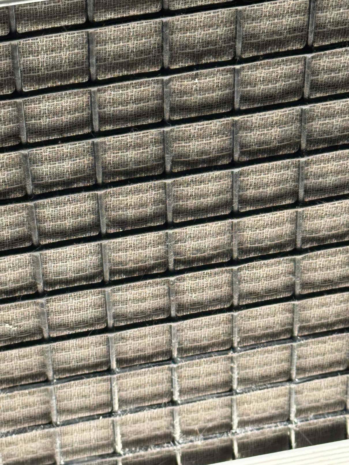 Close-up of condenser coil fins behind a rectangular protective grille on an outdoor unit.