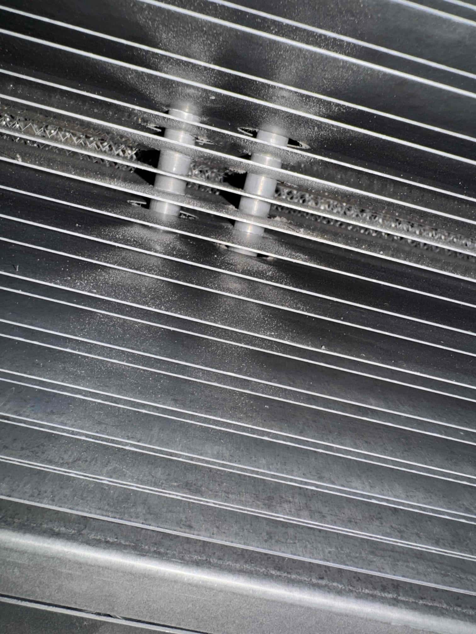 Close-up of a louvered HVAC grille showing two plastic spacers and light dust accumulation around the slats.