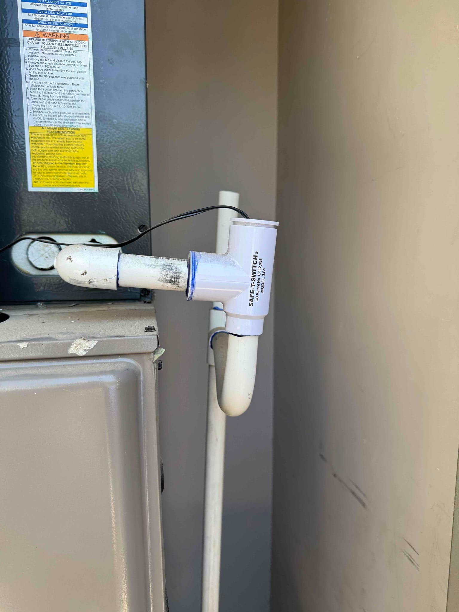 Condensate drain line with a float safety switch installed on a PVC tee beside the air handler.