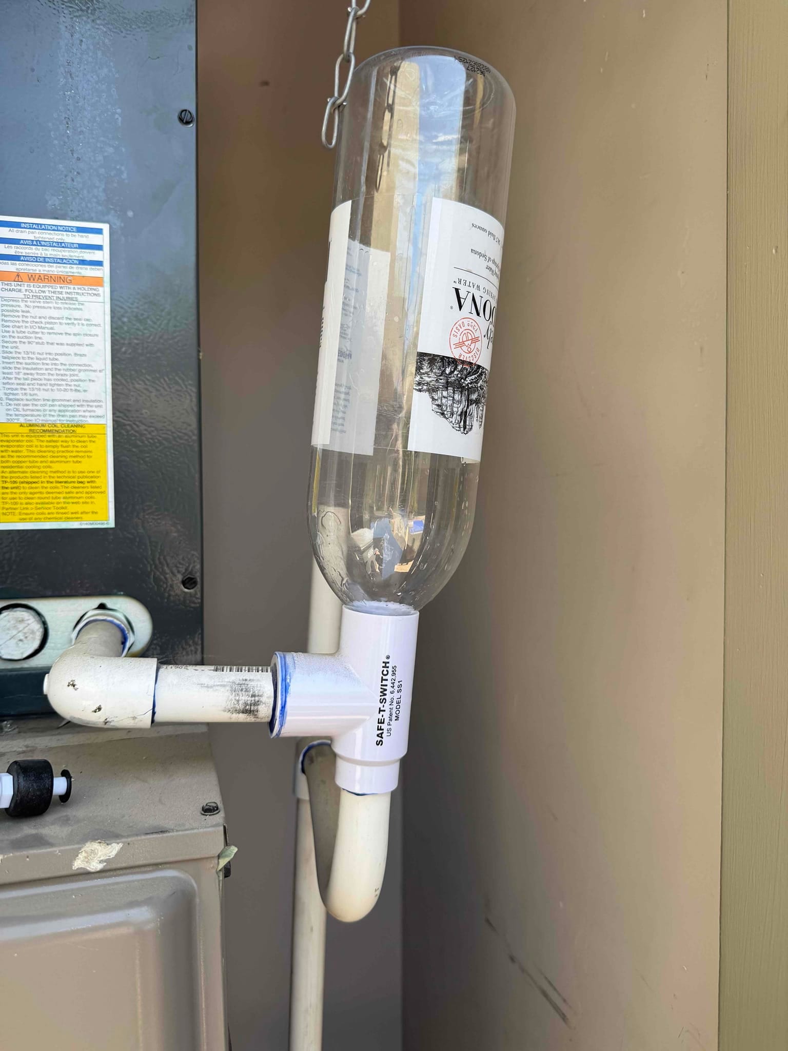 Condensate drain line with a float-switch tee and an inverted plastic bottle attached above near the cabinet.