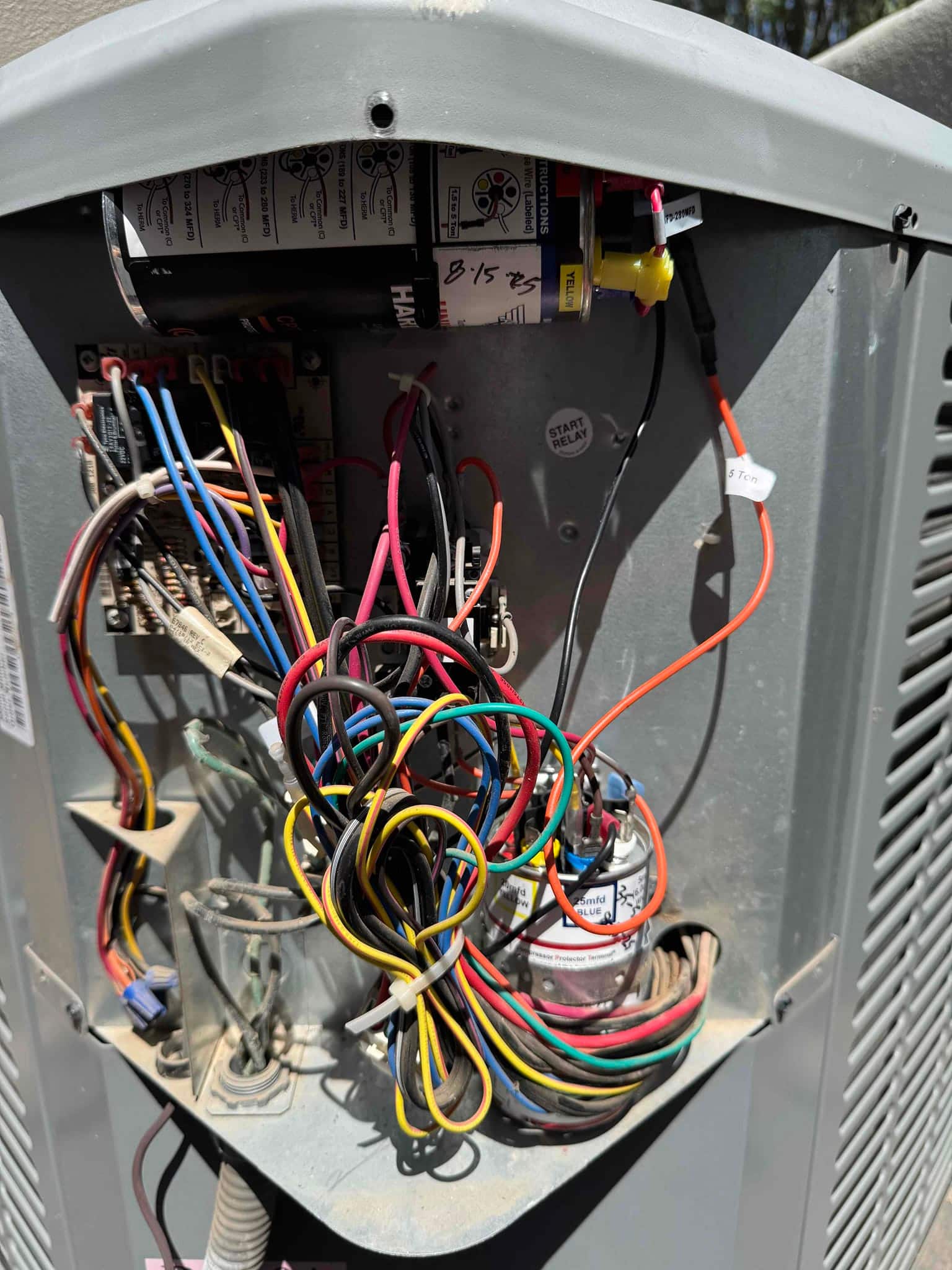 Condenser electrical compartment open, showing capacitors, contactor, start relay, and bundled control wires with dust inside.