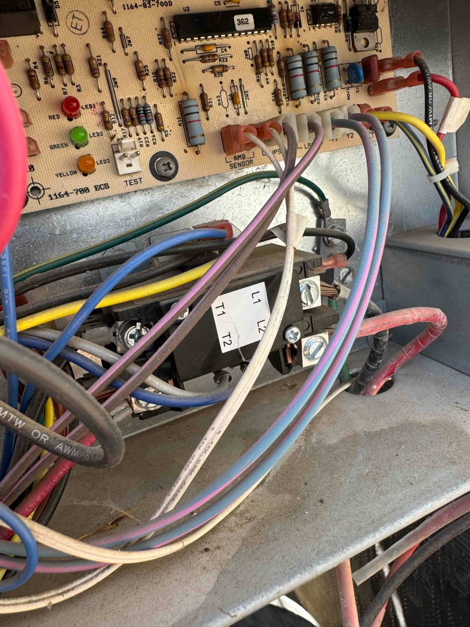 Control board with indicator LEDs and wiring connections above a contactor labeled L1, L2, T1, T2 inside the condenser cabinet.