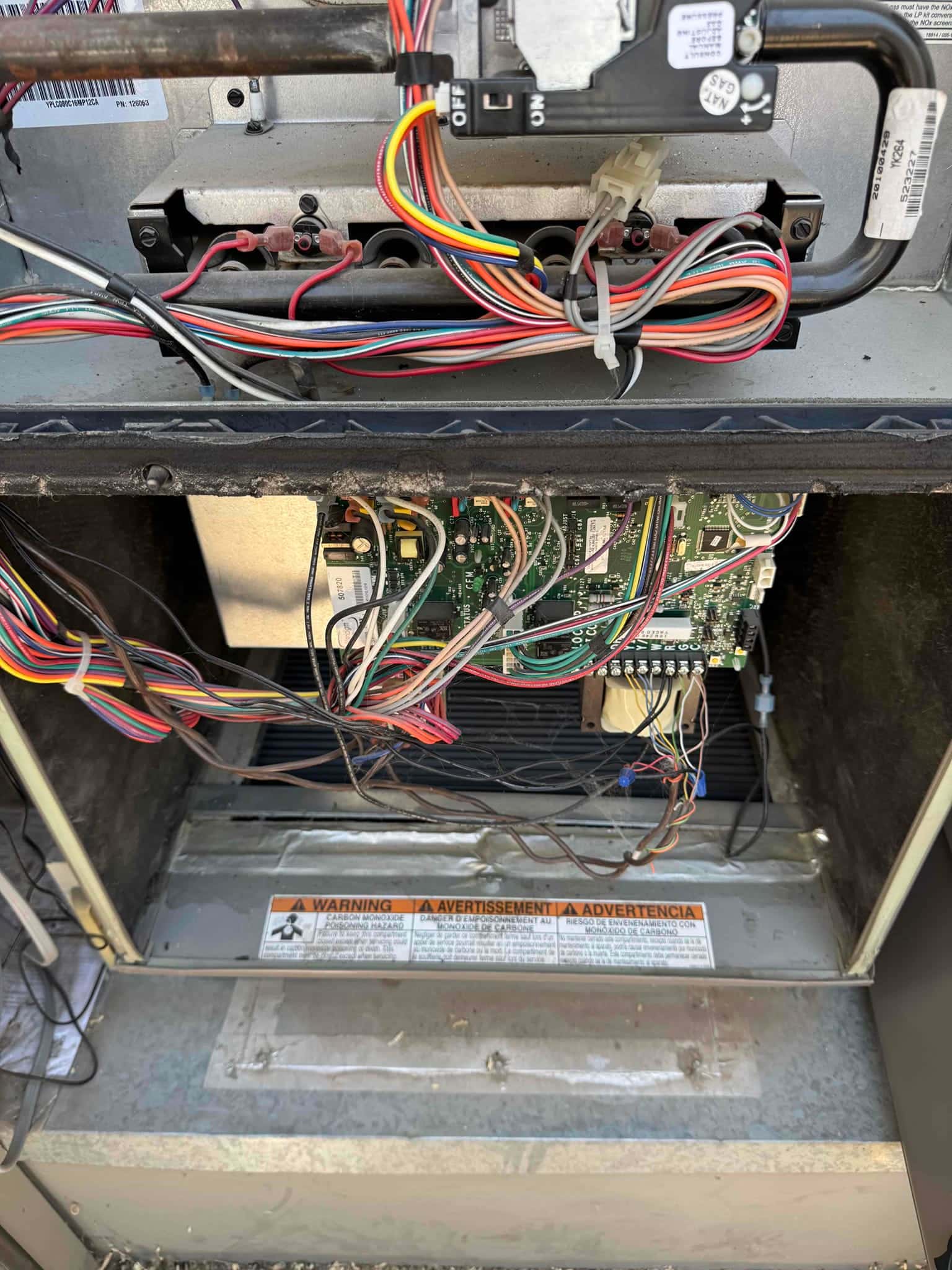 Furnace cabinet open showing gas burner manifold, ignition area, and control board with wiring harness; safety warning label on base.