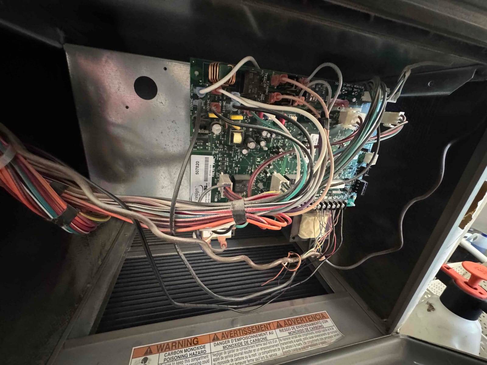 Furnace control board with multiple connected harnesses and wires exposed inside the air handler cabinet.