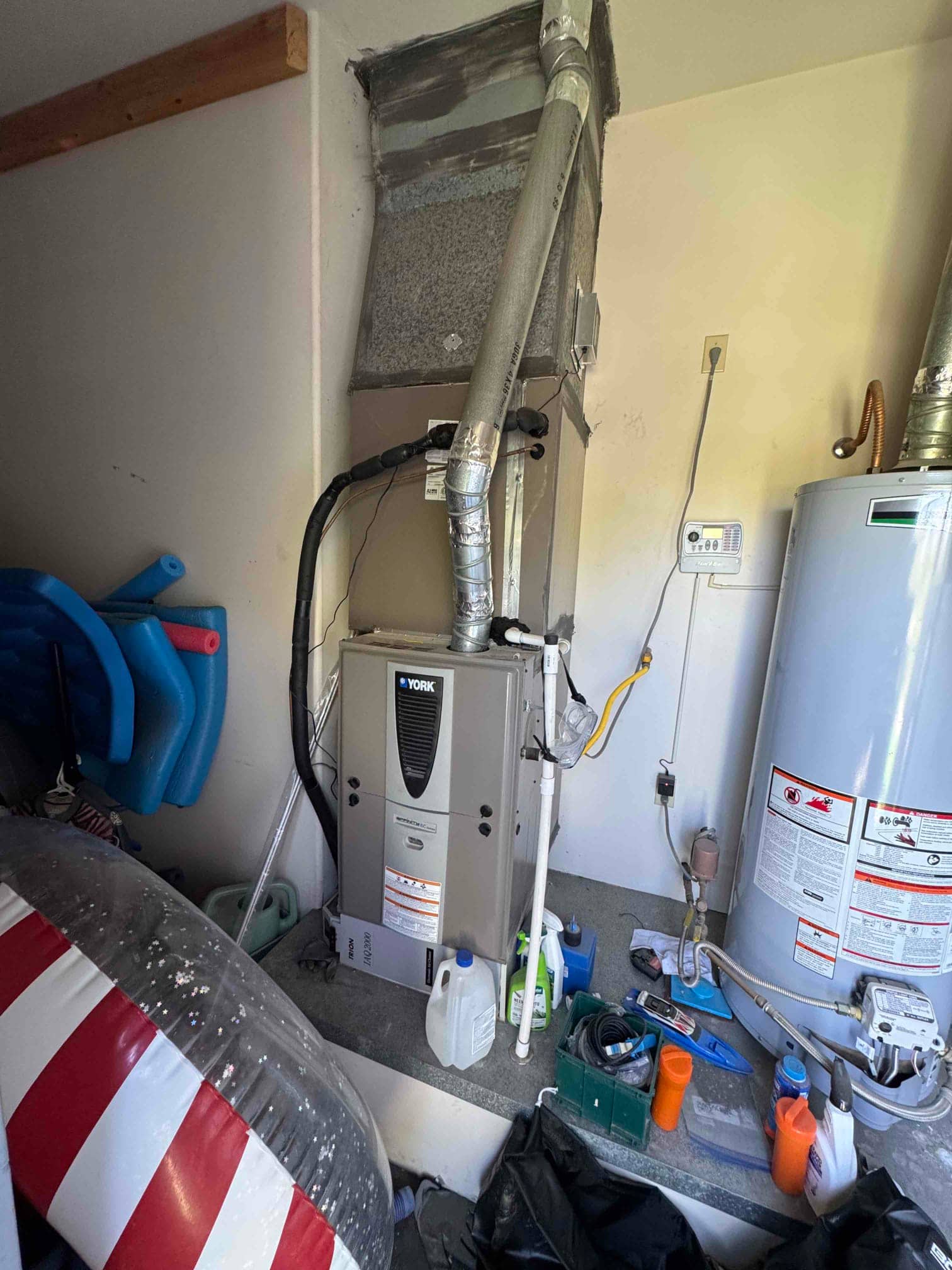 Gas furnace and coil cabinet on a garage platform with flue vent, refrigerant lines, and condensate drain piping visible.