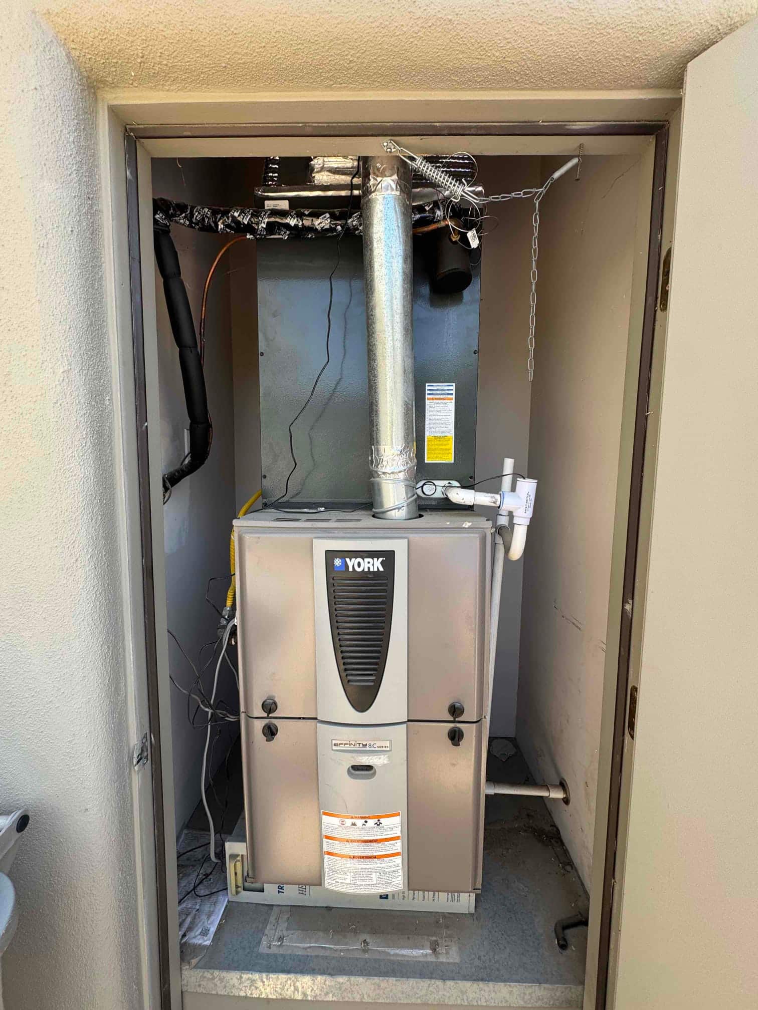Gas furnace and evaporator coil inside an outdoor closet, with flue, condensate drain, and duct connections.