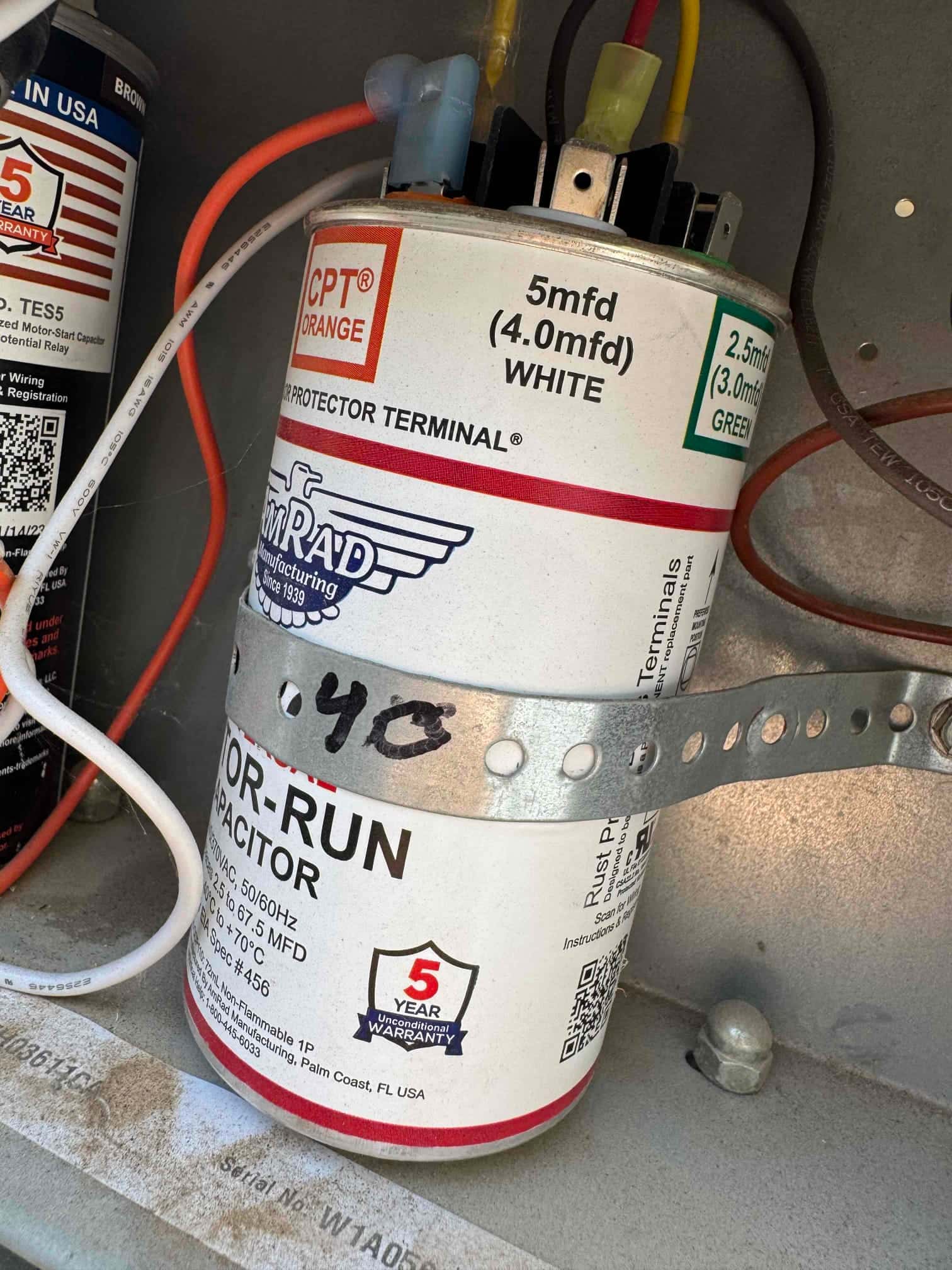 Motor-run capacitor secured with a metal strap, wiring attached, labeled 5 mfd WHITE and 2.5 mfd GREEN.