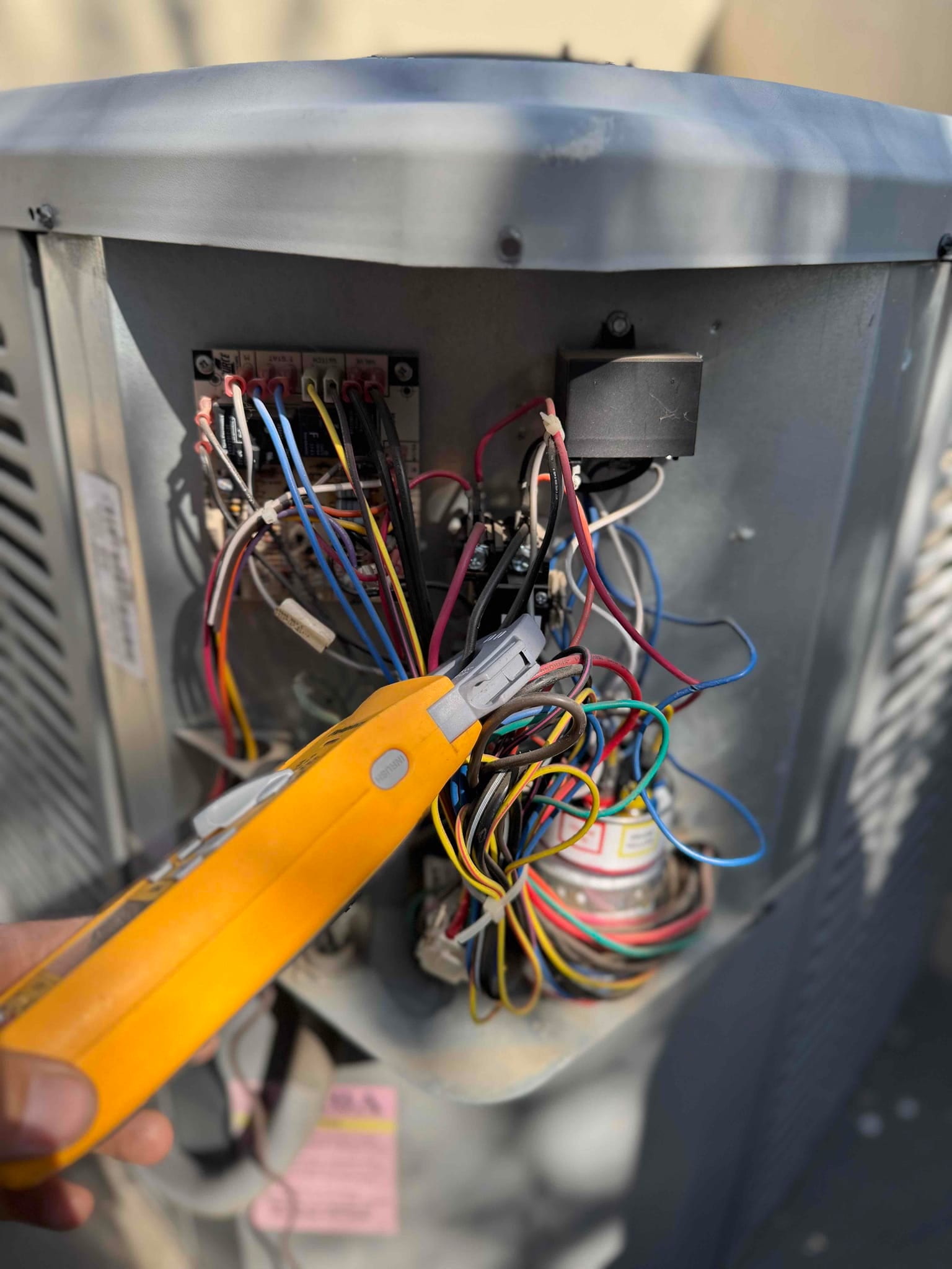 Open condenser control compartment shows wiring on a terminal block, a cylindrical capacitor, and a non-contact voltage tester in use.