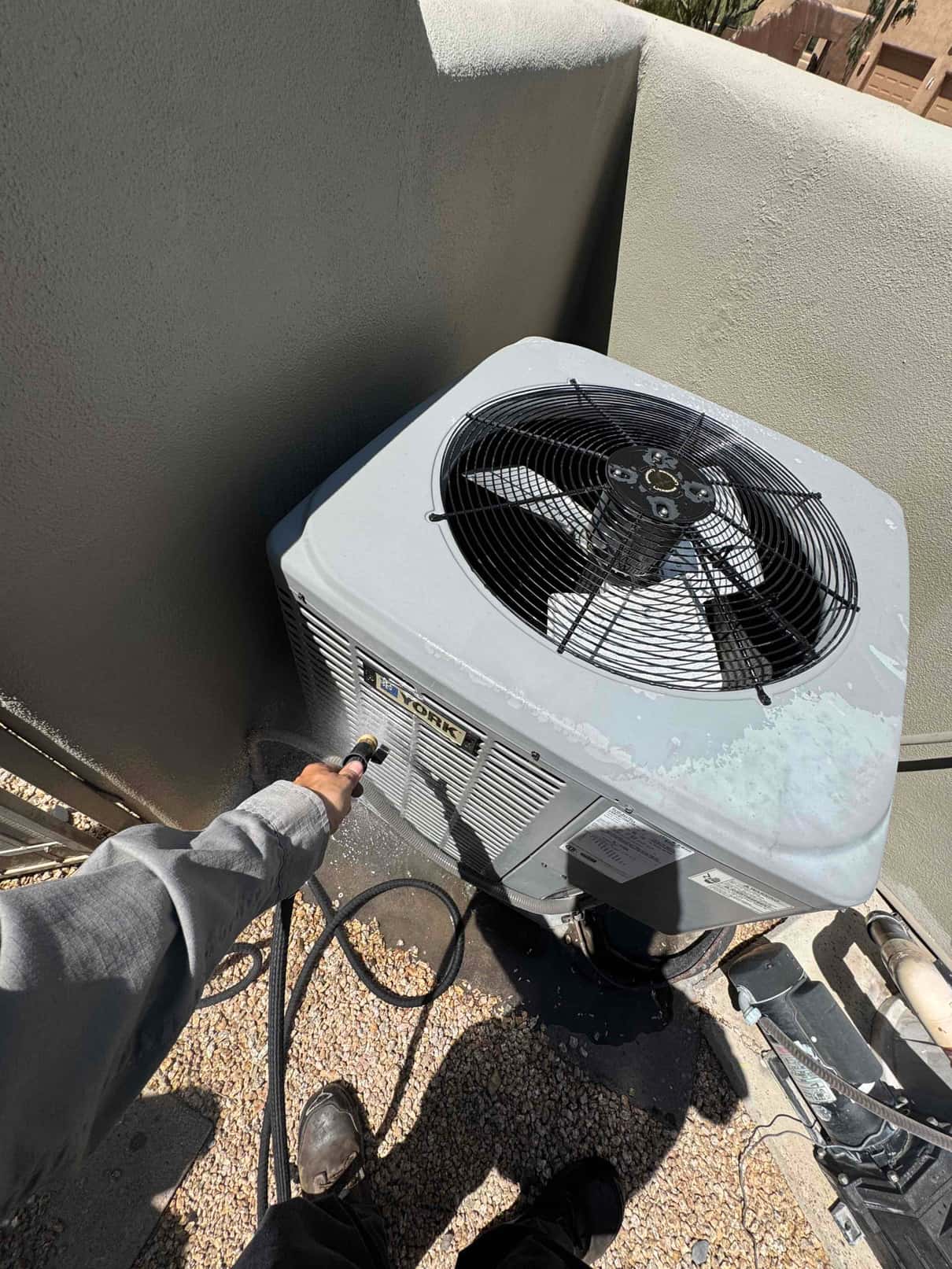Outdoor condenser with peeling paint on top as the technician sprays water onto the coil.