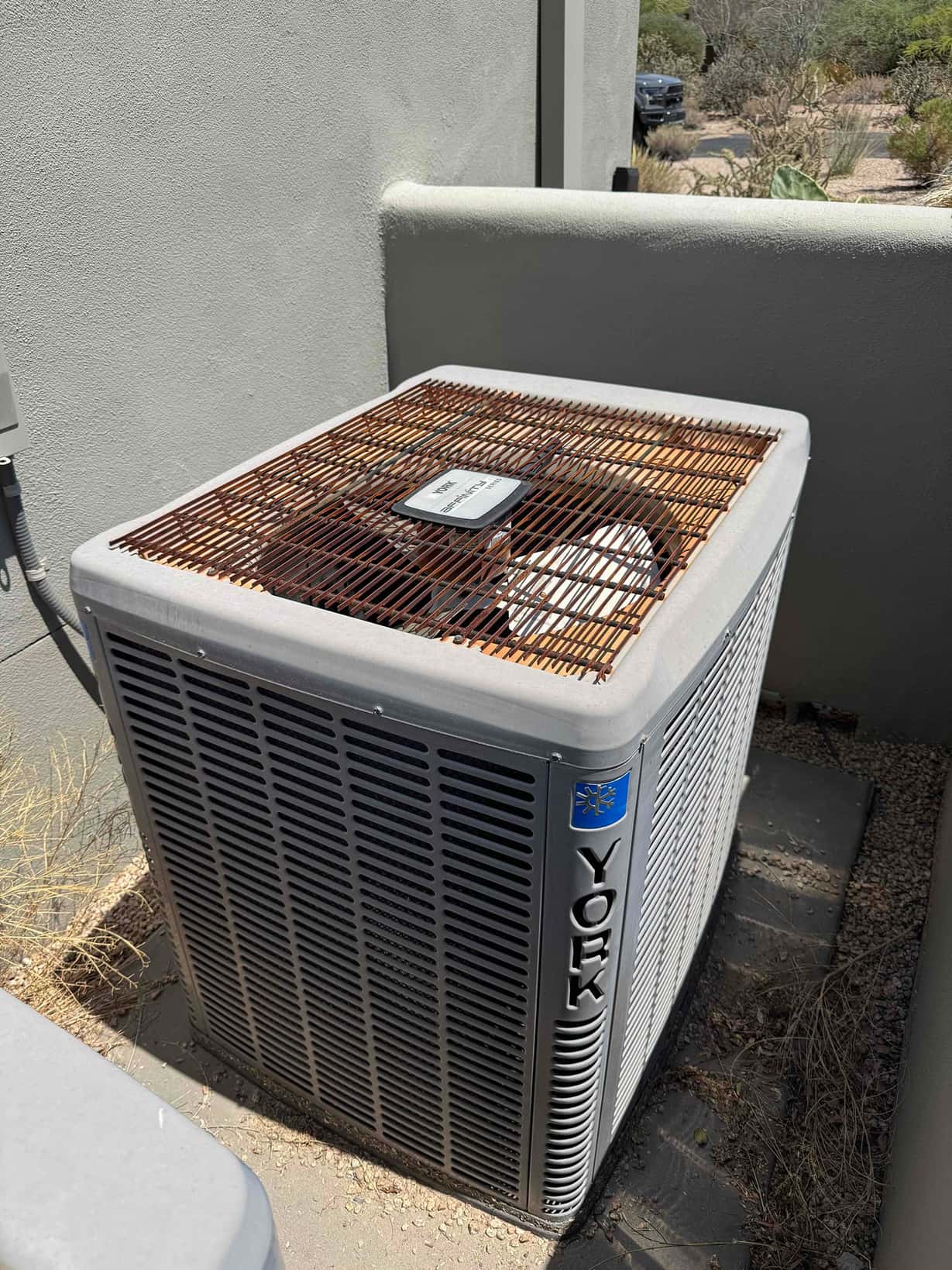 Outdoor condenser unit beside a wall; top grille shows heavy rust and surface corrosion.