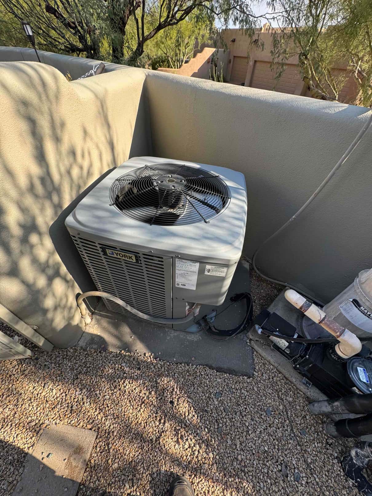 Outdoor condenser unit on rooftop corner with service access panel and flexible conduit connected; surrounding tools and hoses nearby.