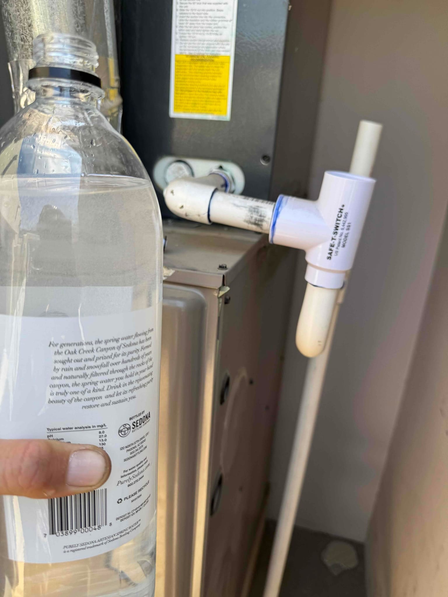 PVC condensate drain with tee-style float safety switch next to an indoor air handler cabinet.