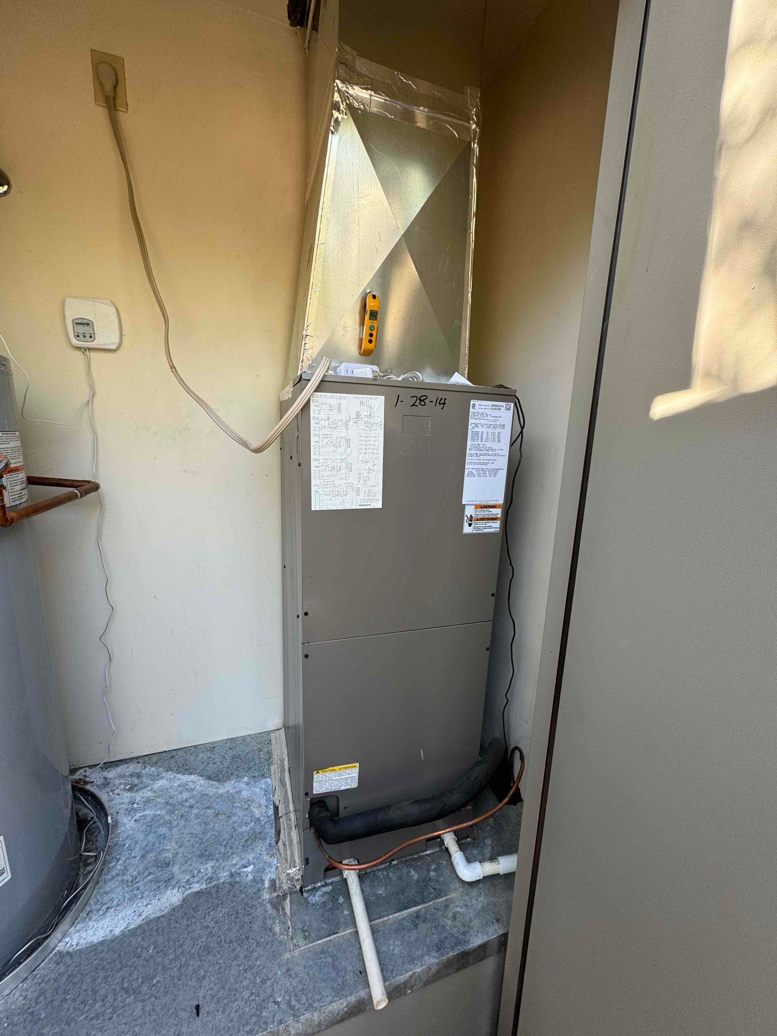 Residential air handler with insulated refrigerant line and PVC condensate drain, with sealed duct plenum above and wall thermostat nearby.