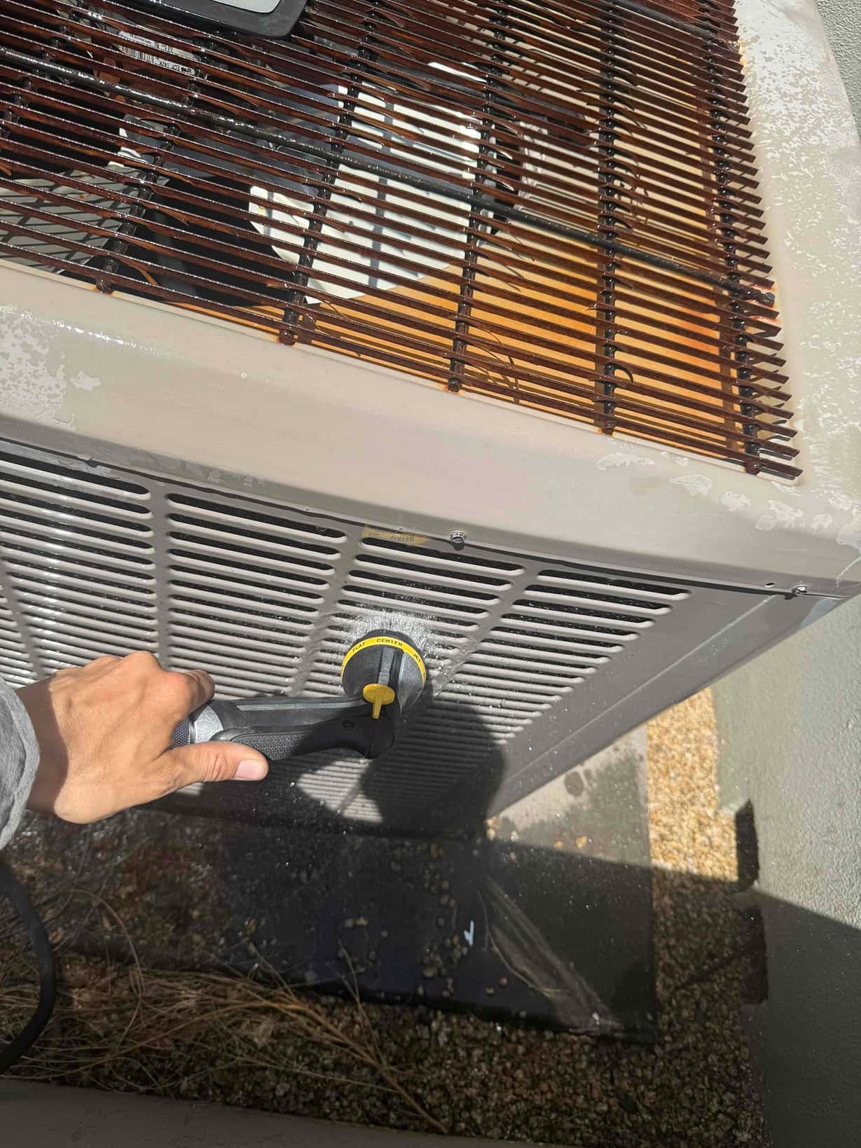 Technician uses hose nozzle to rinse debris from the side panels of an outdoor condenser.