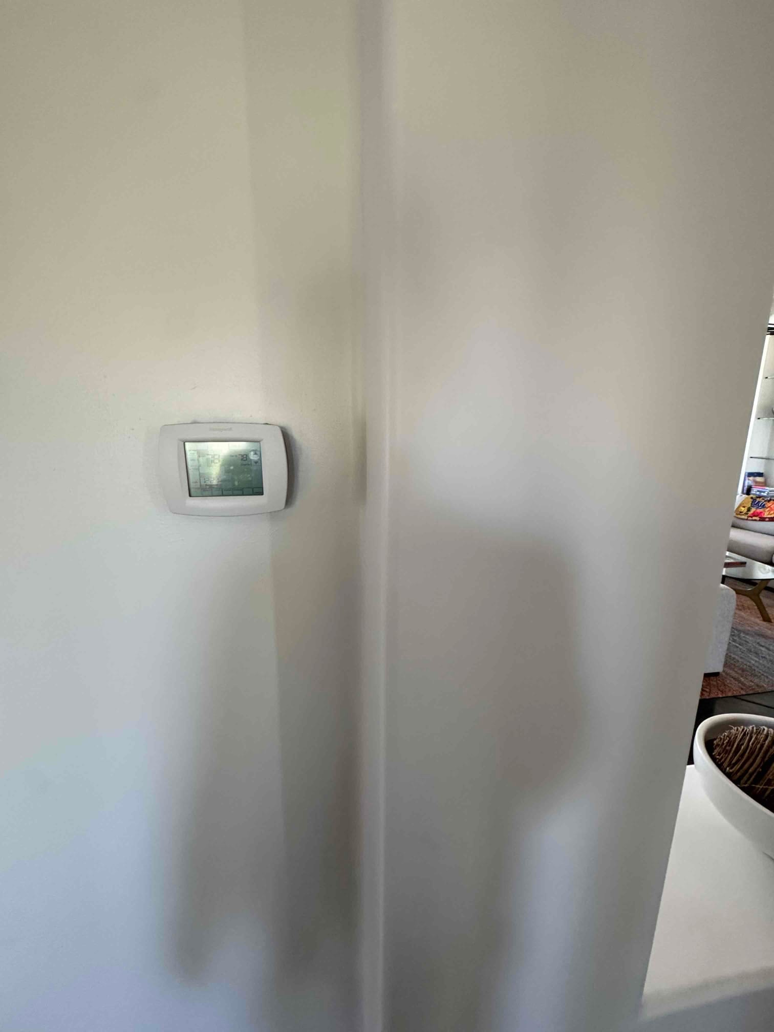 Wall-mounted digital thermostat on an interior partition, backlit display active with basic temperature and mode indicators visible.