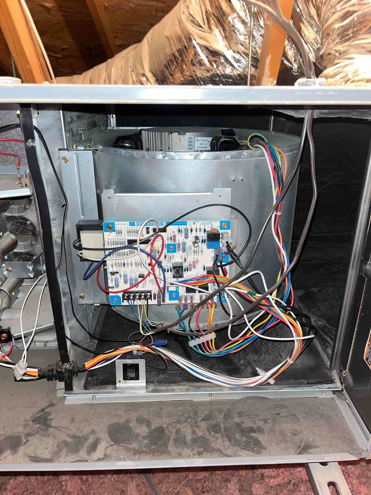 Air handler blower compartment open, showing control board with multiple connected wires and the blower housing in the attic.