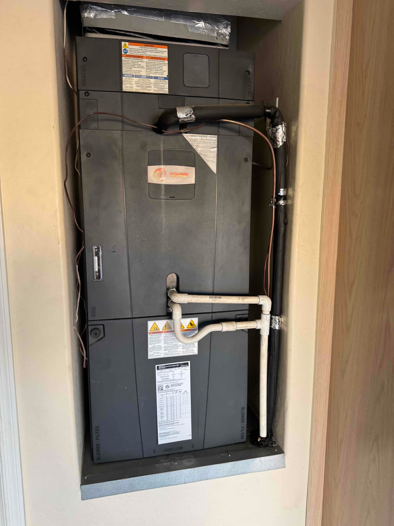 Air handler in a closet with insulated refrigerant lines and PVC condensate drain piping connected.