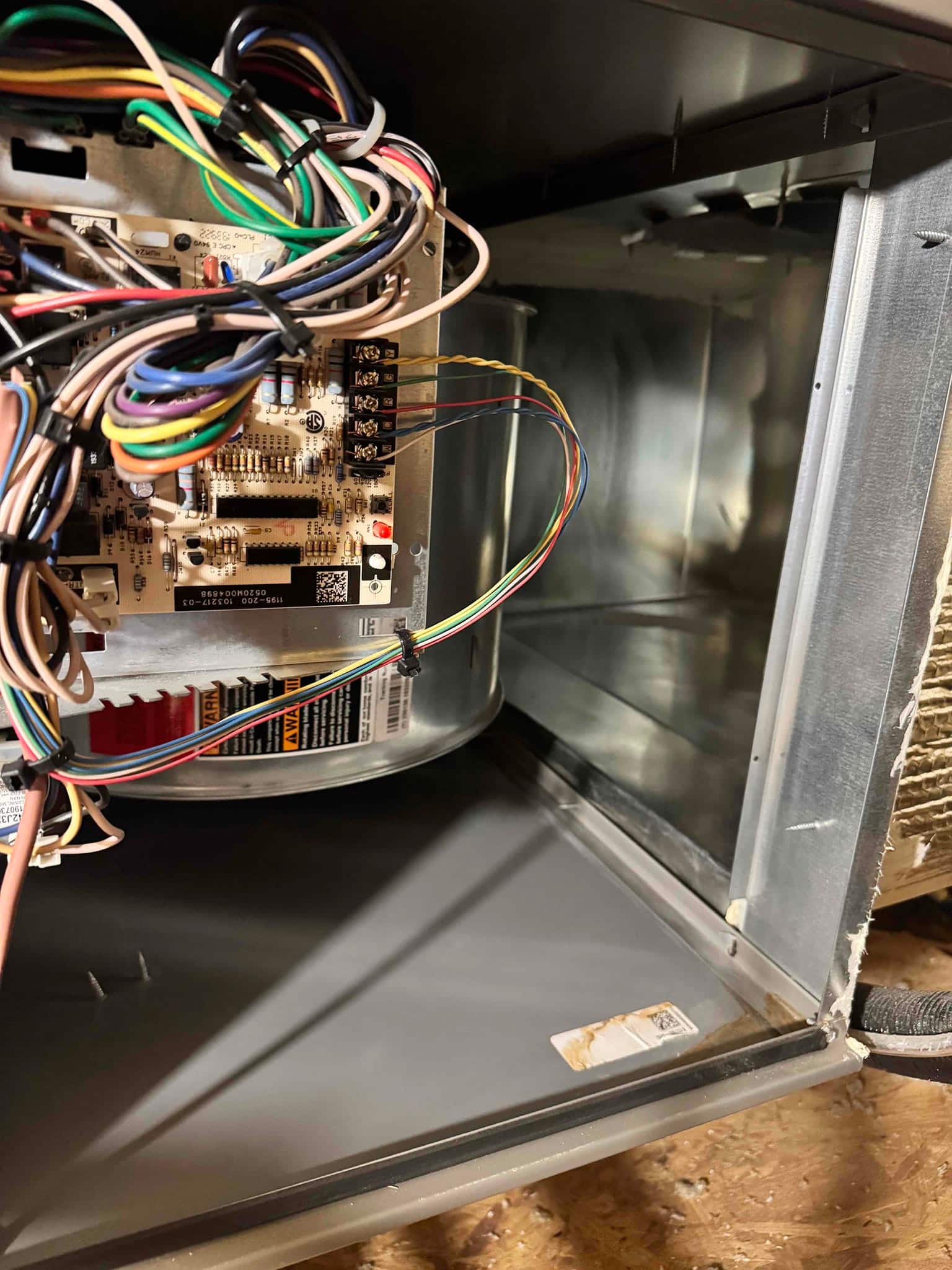 Air handler compartment open, showing control board with wiring and blower housing next to galvanized duct.