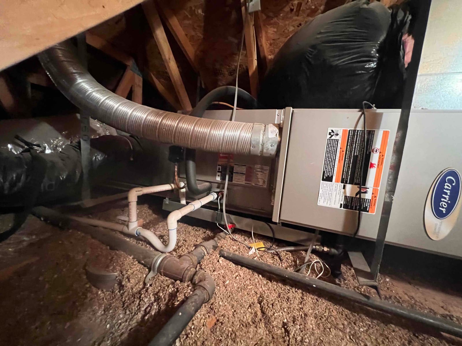 Attic air handler with flexible duct connections, condensate drain piping, and gas line visible around the unit.