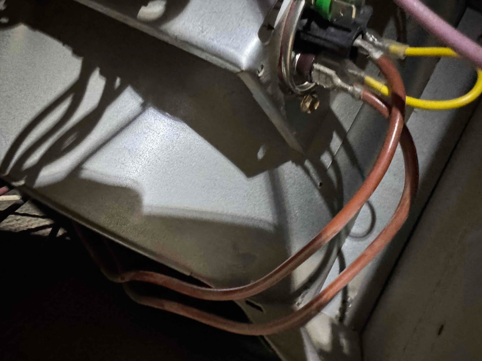 Close-up of wiring connected to a round metal fitting on a panel, with copper tubing loops inside the unit.