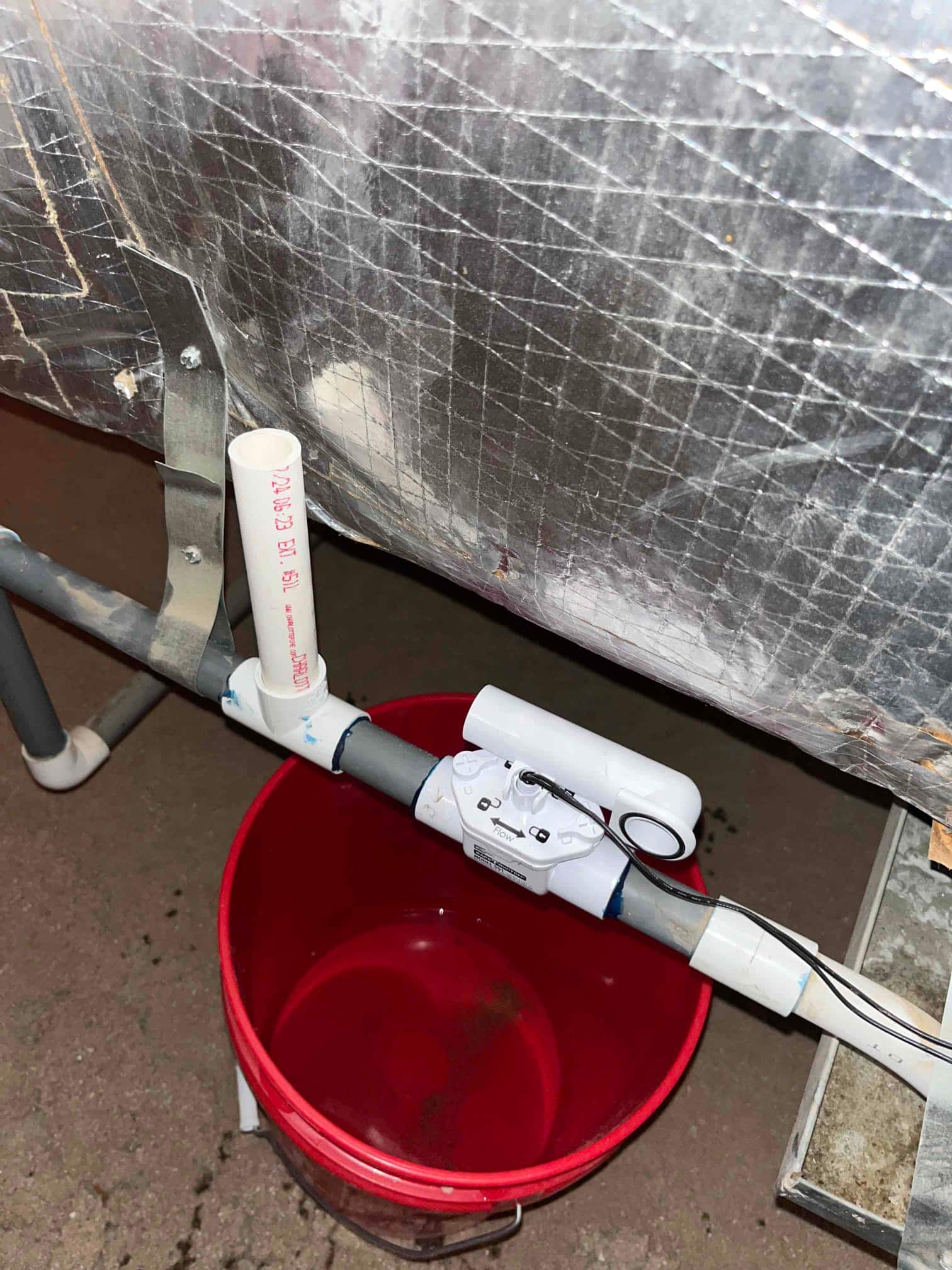 Condensate drain line with an inline float safety switch installed, positioned above a red collection bucket.