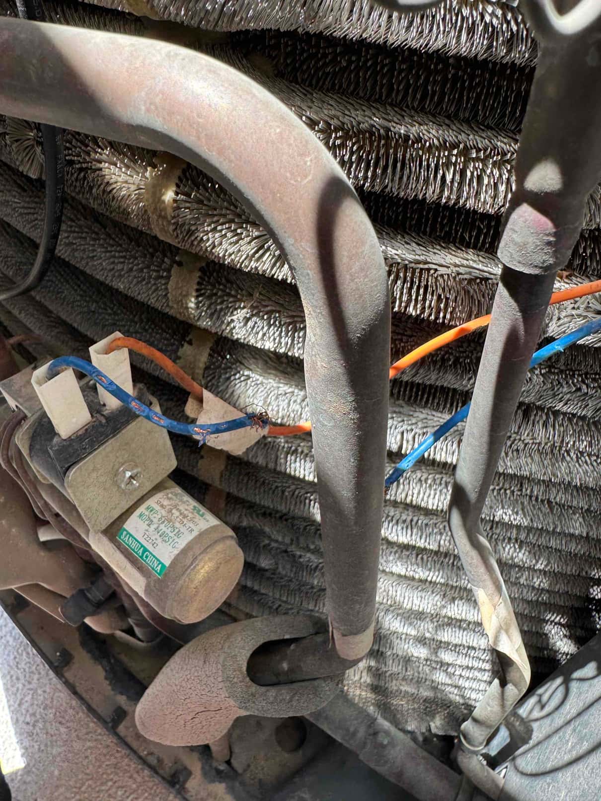 Condenser coil and refrigerant lines inside outdoor unit, showing dust-covered cylindrical component and connected wiring.