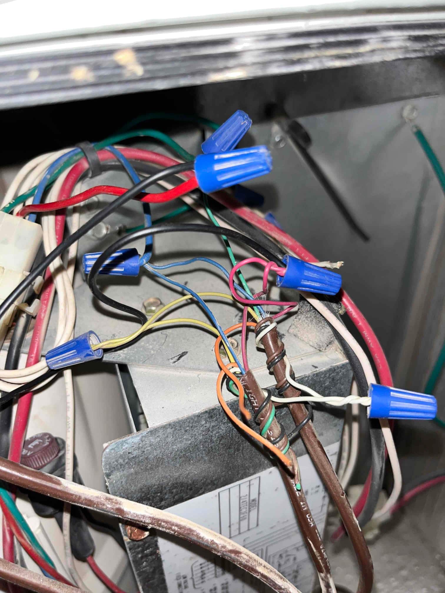 Control compartment wiring with multiple wire nuts and a mounted transformer, showing mixed colored conductors and dust.