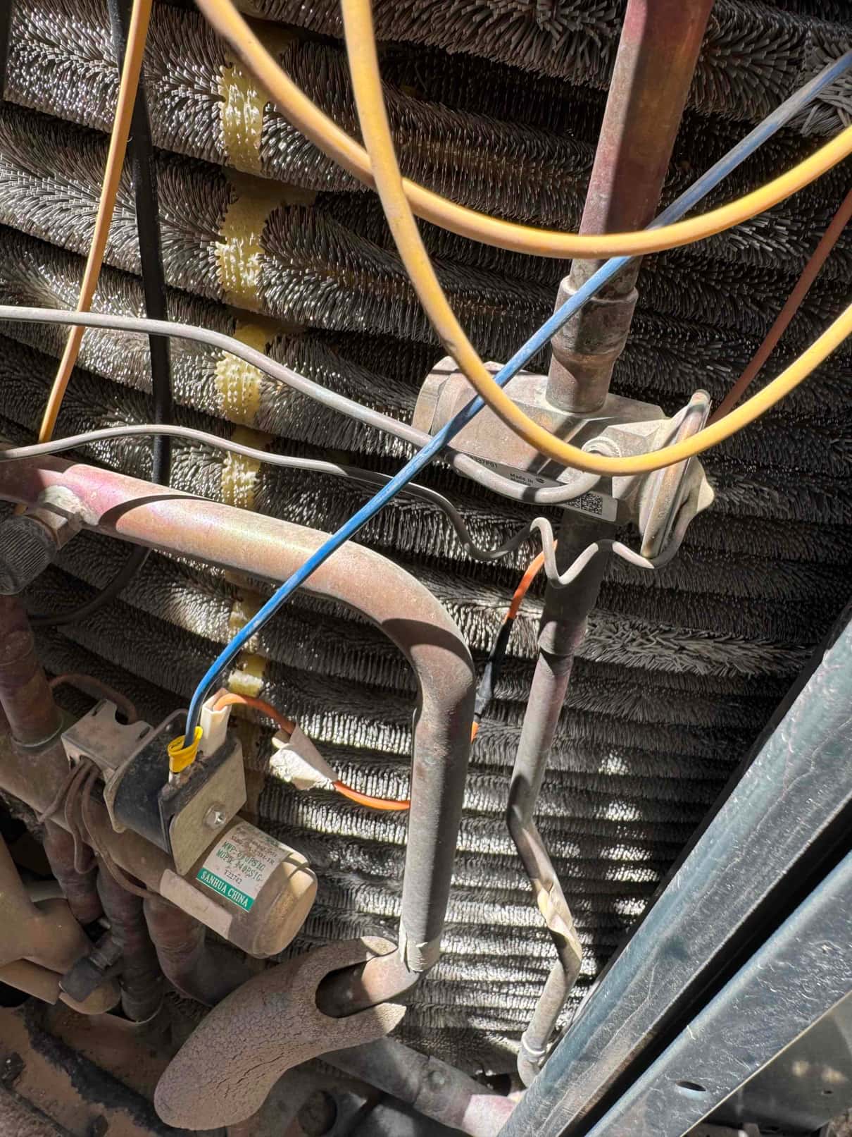 Copper refrigerant lines, coil fins, and control wiring inside an outdoor condenser unit with visible insulation.