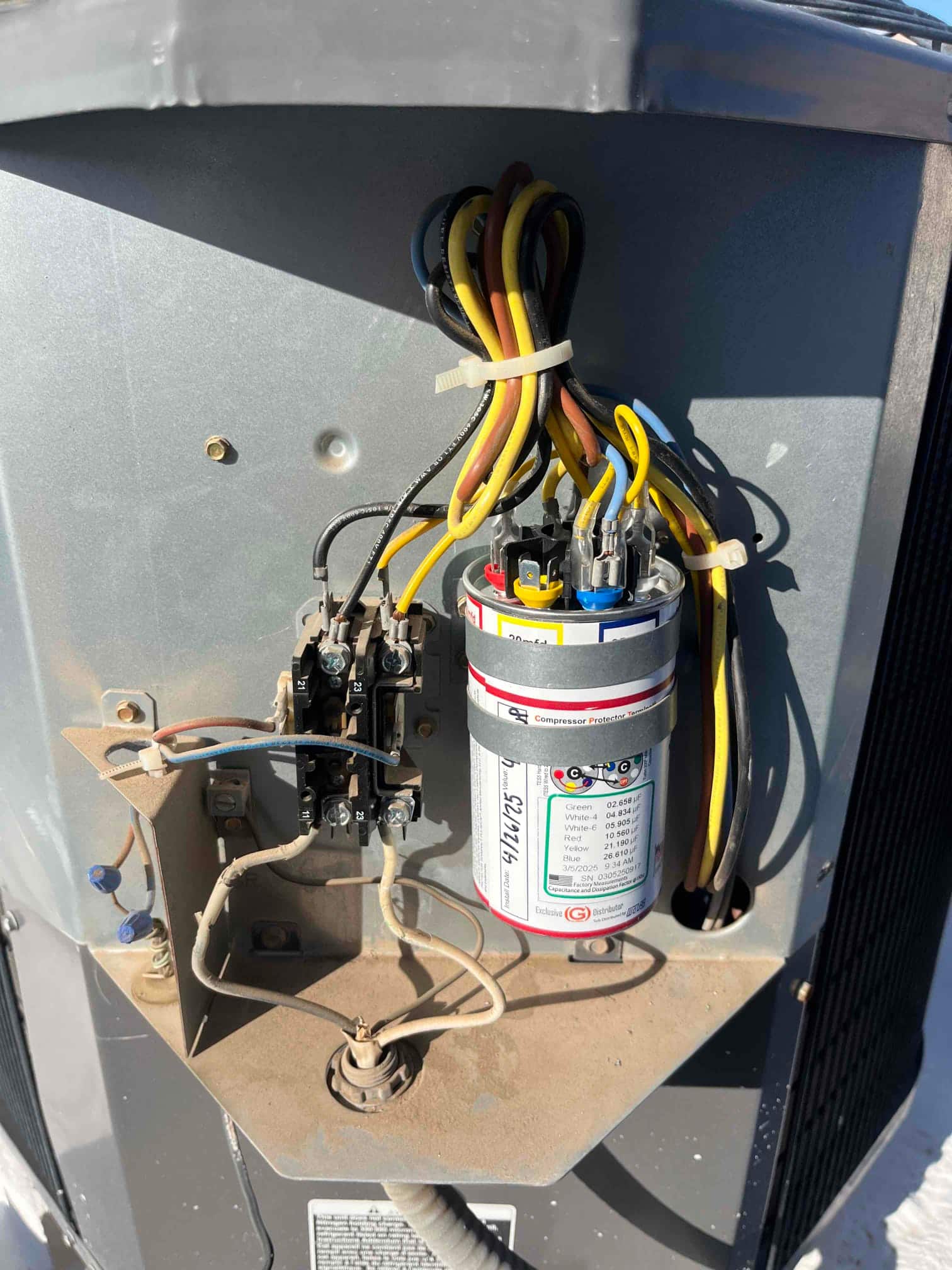 Dual-run capacitor with wiring connected beside a two-pole contactor inside the outdoor condenser control compartment.