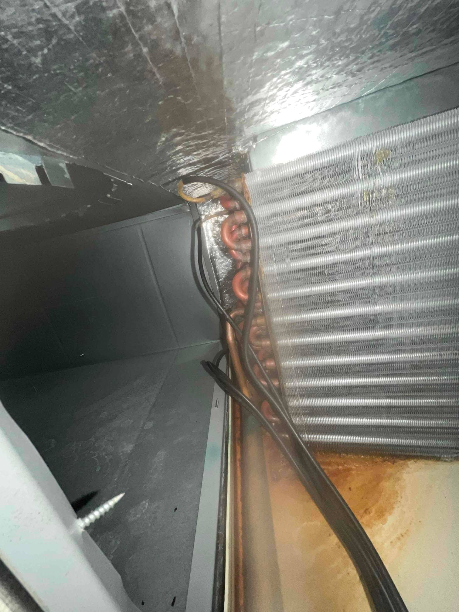Evaporator coil and copper tubing inside air handler cabinet with wiring, above a drain pan showing brown discoloration.