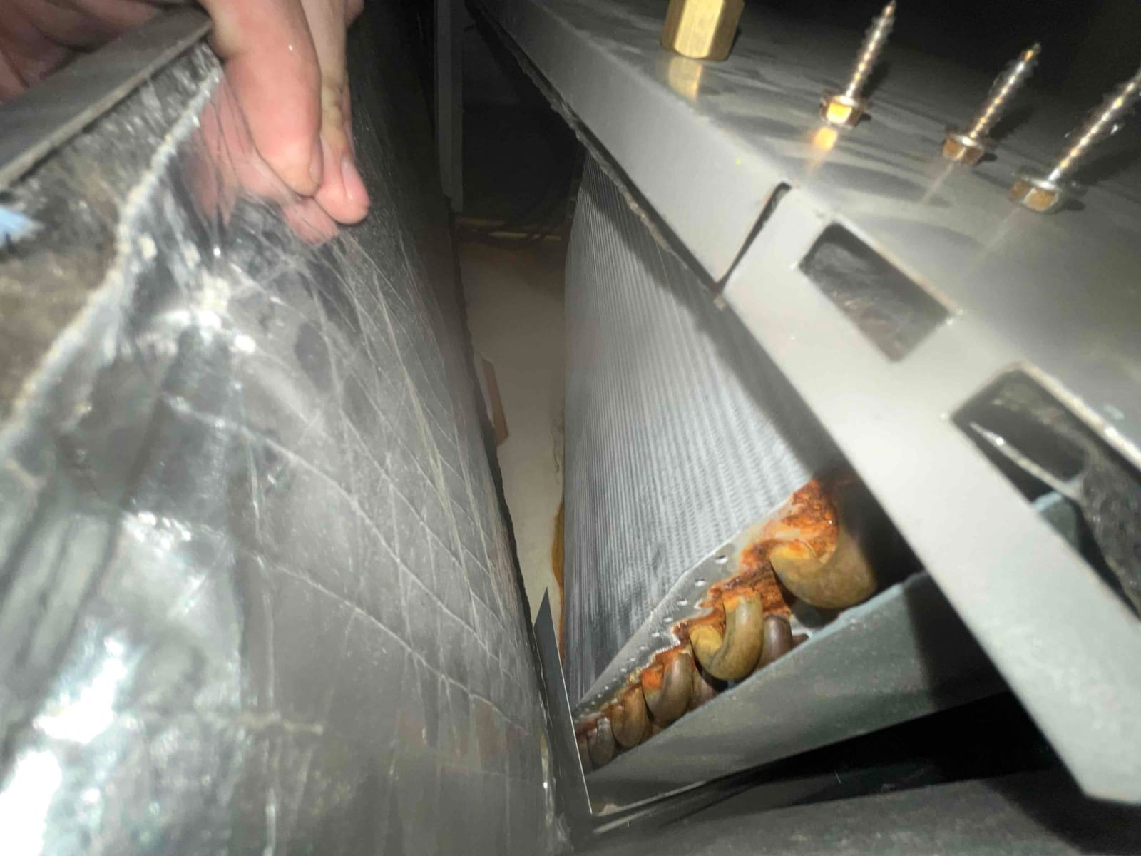 Evaporator coil inside the air handler, with copper U-bends showing orange rust and nearby sheet-metal housing.