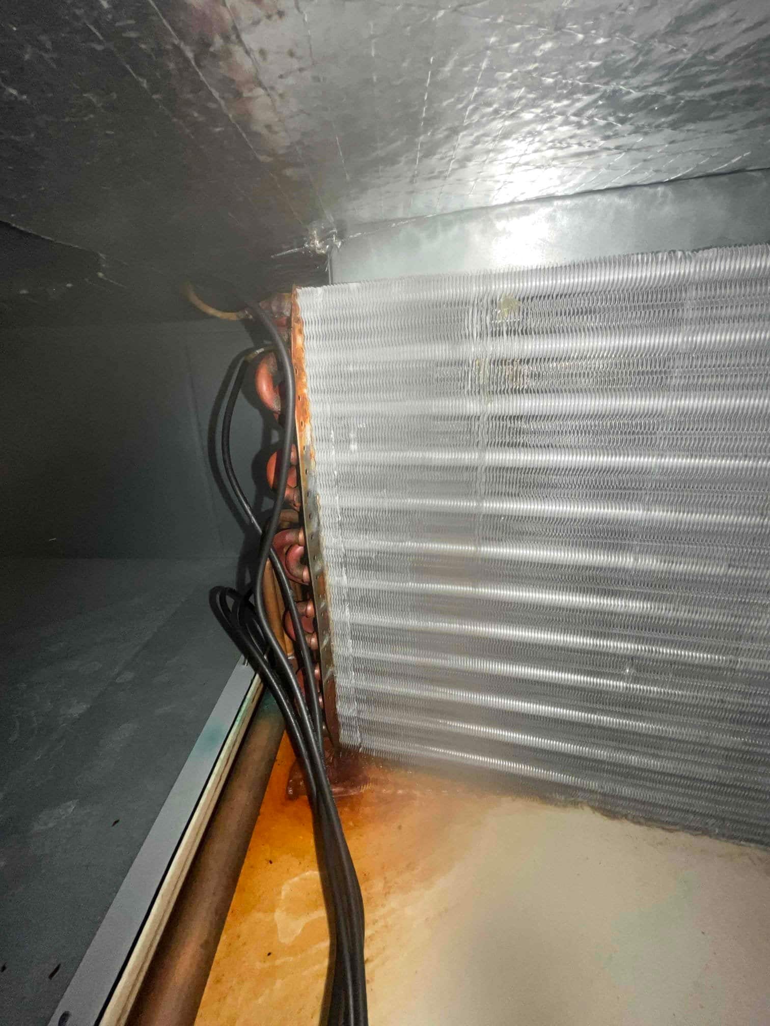 Evaporator coil inside air handler, with copper tubing and rust-colored staining in the drain pan.