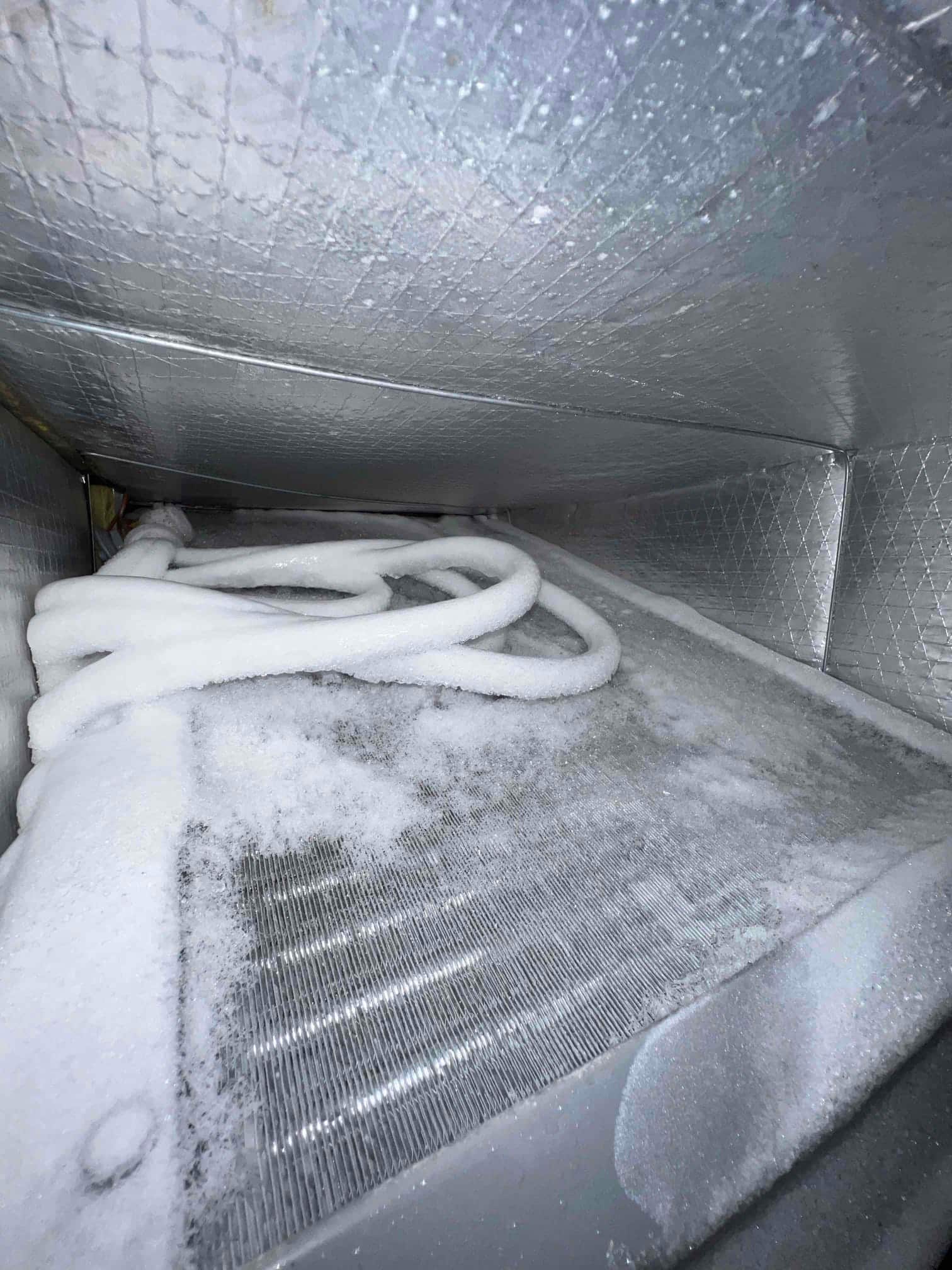 Evaporator coil and refrigerant lines inside air handler covered in frost and ice buildup.