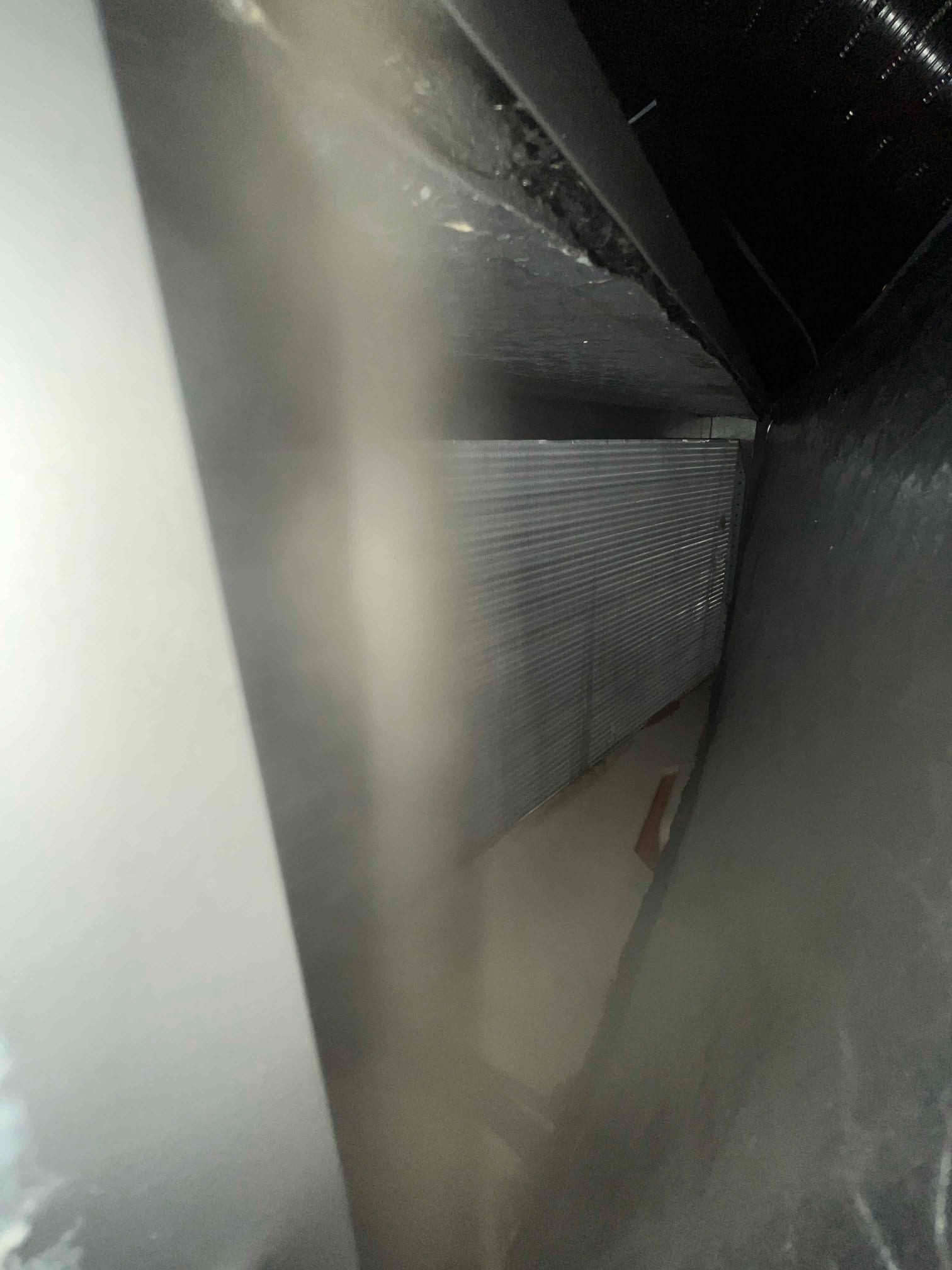 Finned coil surface inside the air handler cabinet, viewed through a narrow gap with surrounding sheet metal.
