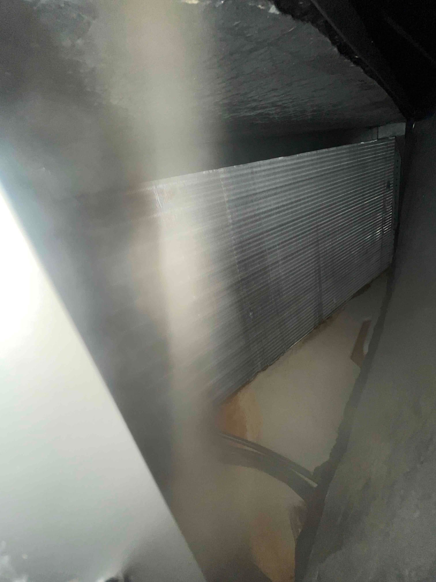 Finned HVAC coil surface inside a duct plenum, with sheet metal walls and interior surfaces visible along the edges.