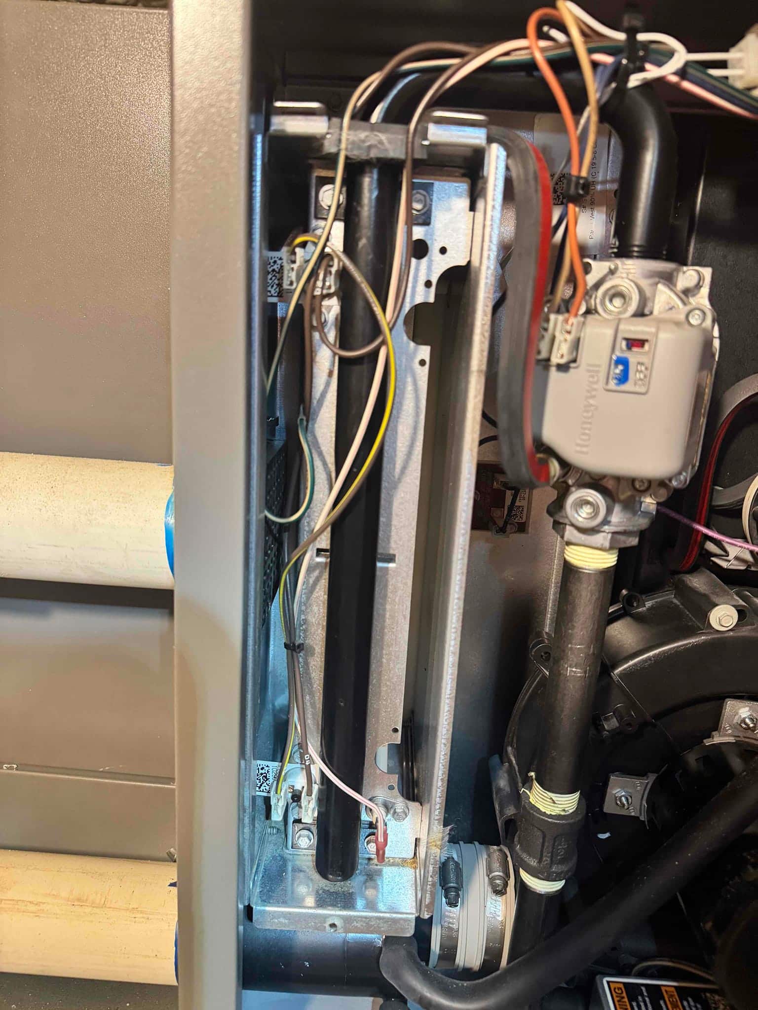 Furnace burner compartment with gas valve, burner tubes, ignition components, wiring connections, and adjacent black gas piping and housing.