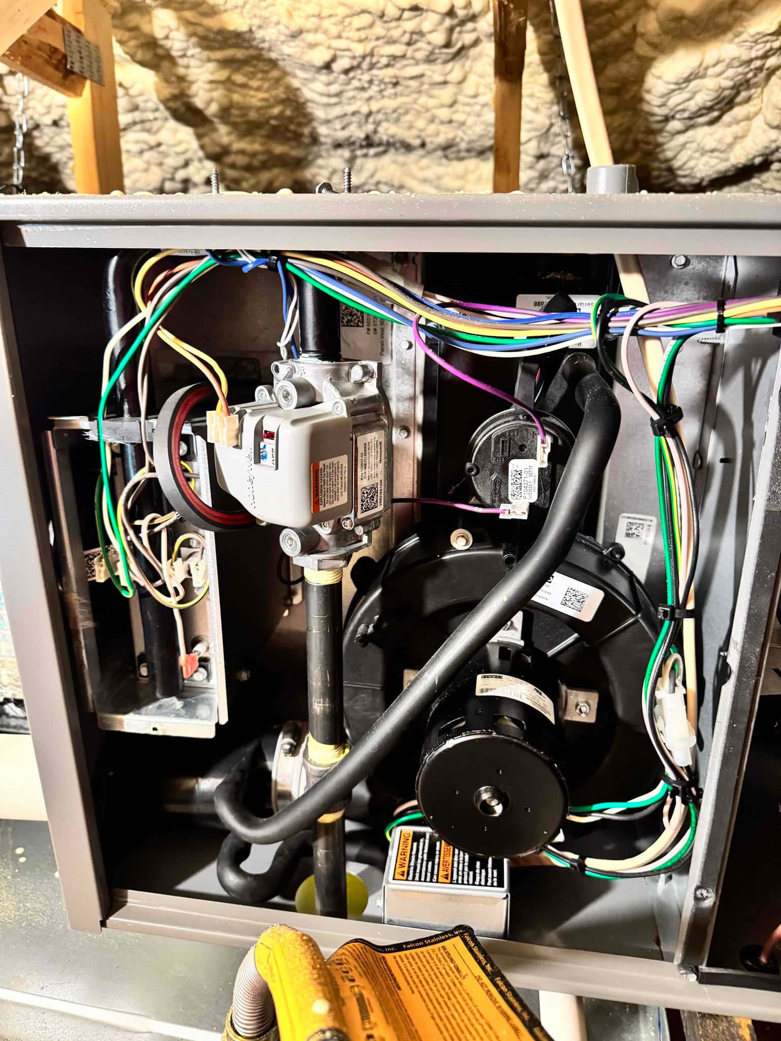 Furnace cabinet open, showing gas valve, inducer motor, wiring harnesses, and condensate drain tubing inside the indoor unit.